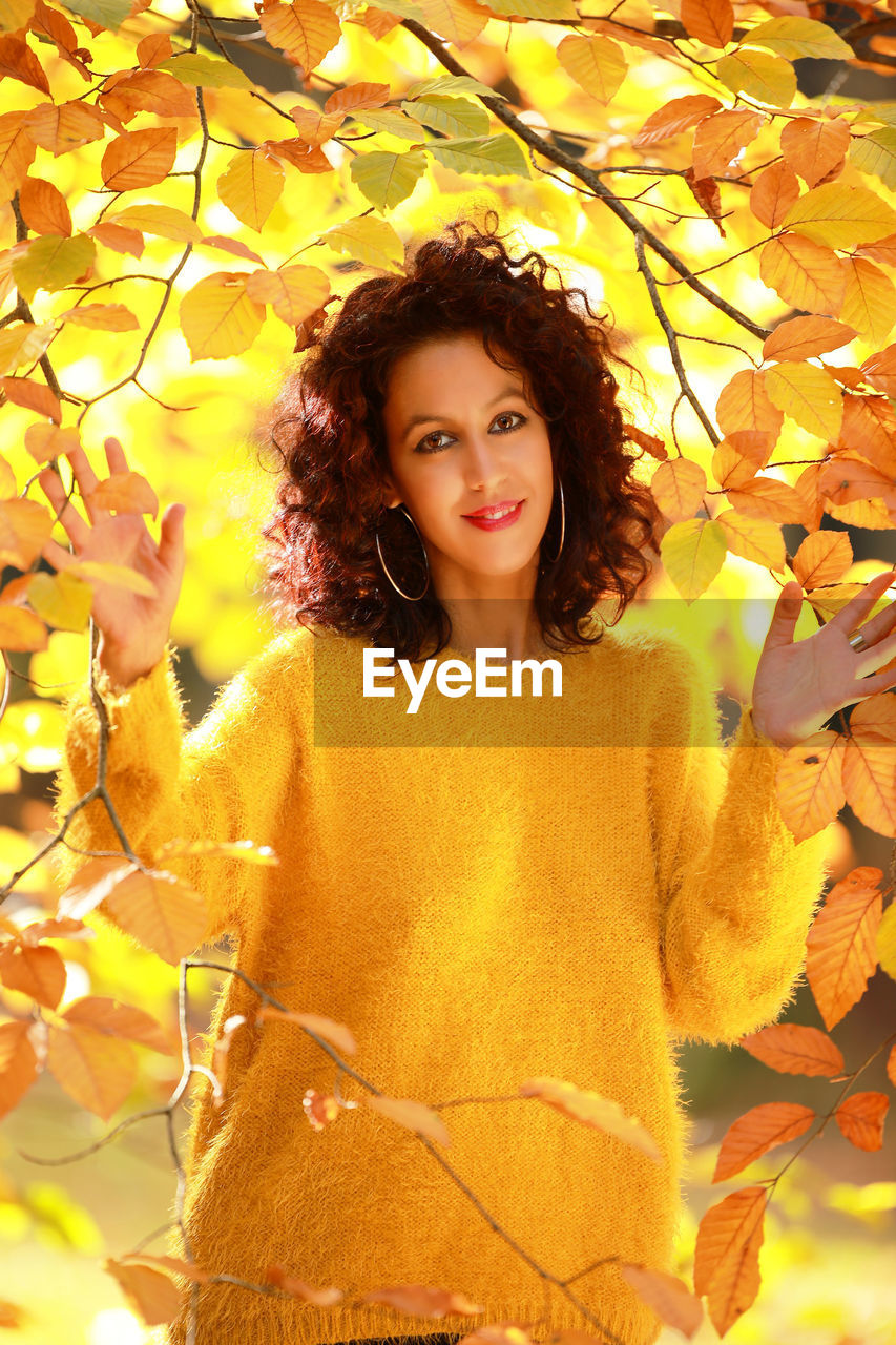 PORTRAIT OF YOUNG WOMAN STANDING BY AUTUMN LEAVES