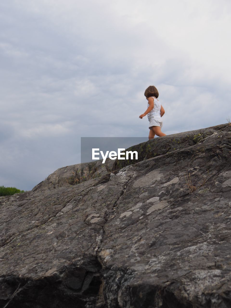 Low angle view of girl walking on rock against sky