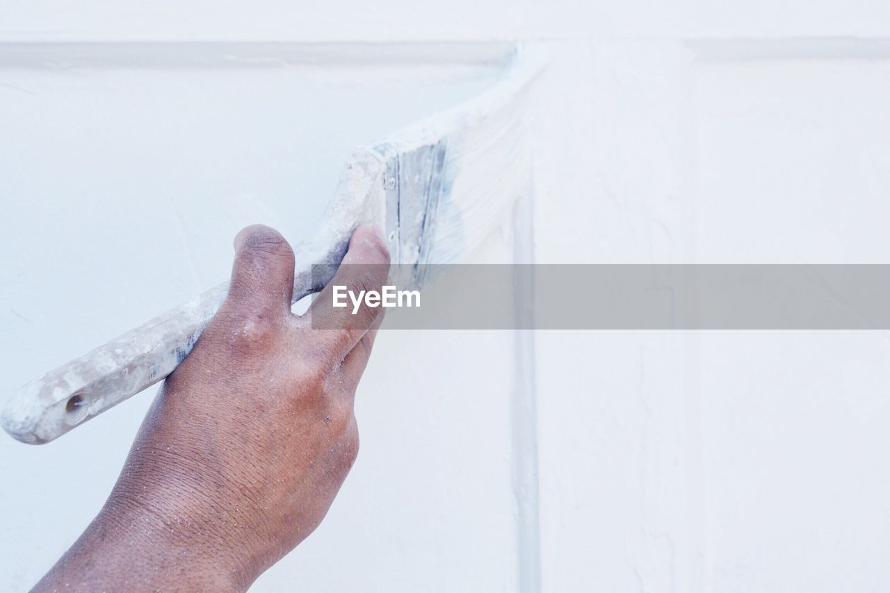 Cropped hand of person painting white wall