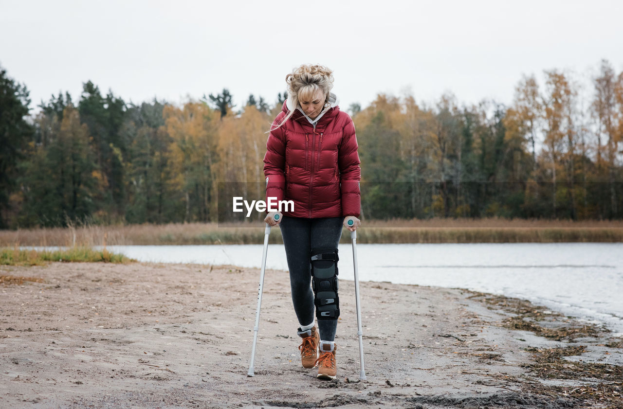 Injured woman walking with crutches on the beach looking thoughtful