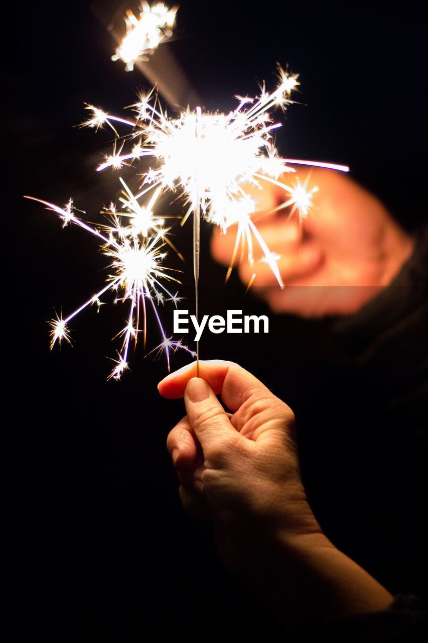 Hands holding sparklers against black background