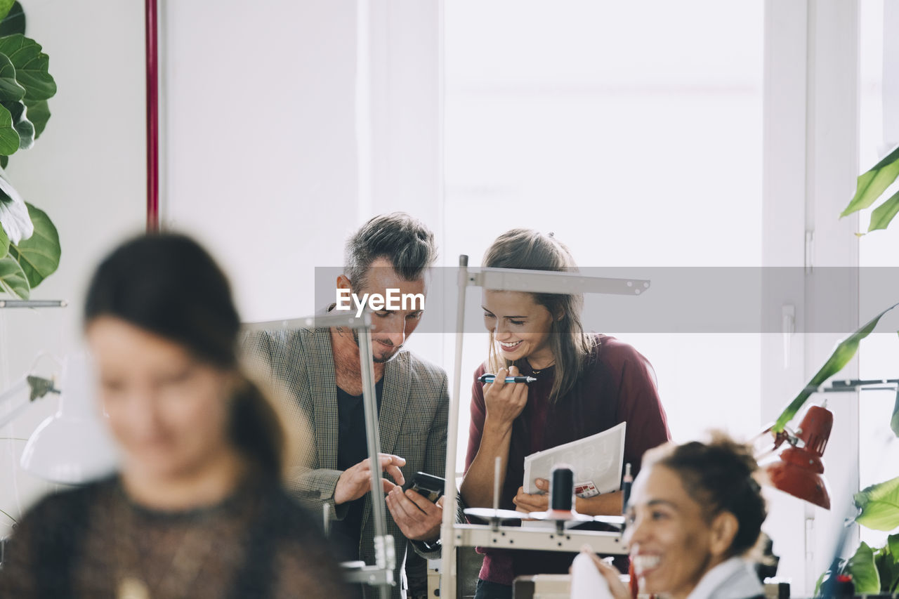 Smiling business professionals discussing over mobile phone in office