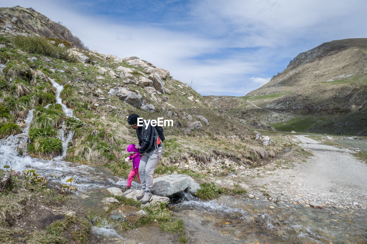 MAN STANDING ON ROCK AGAINST MOUNTAIN