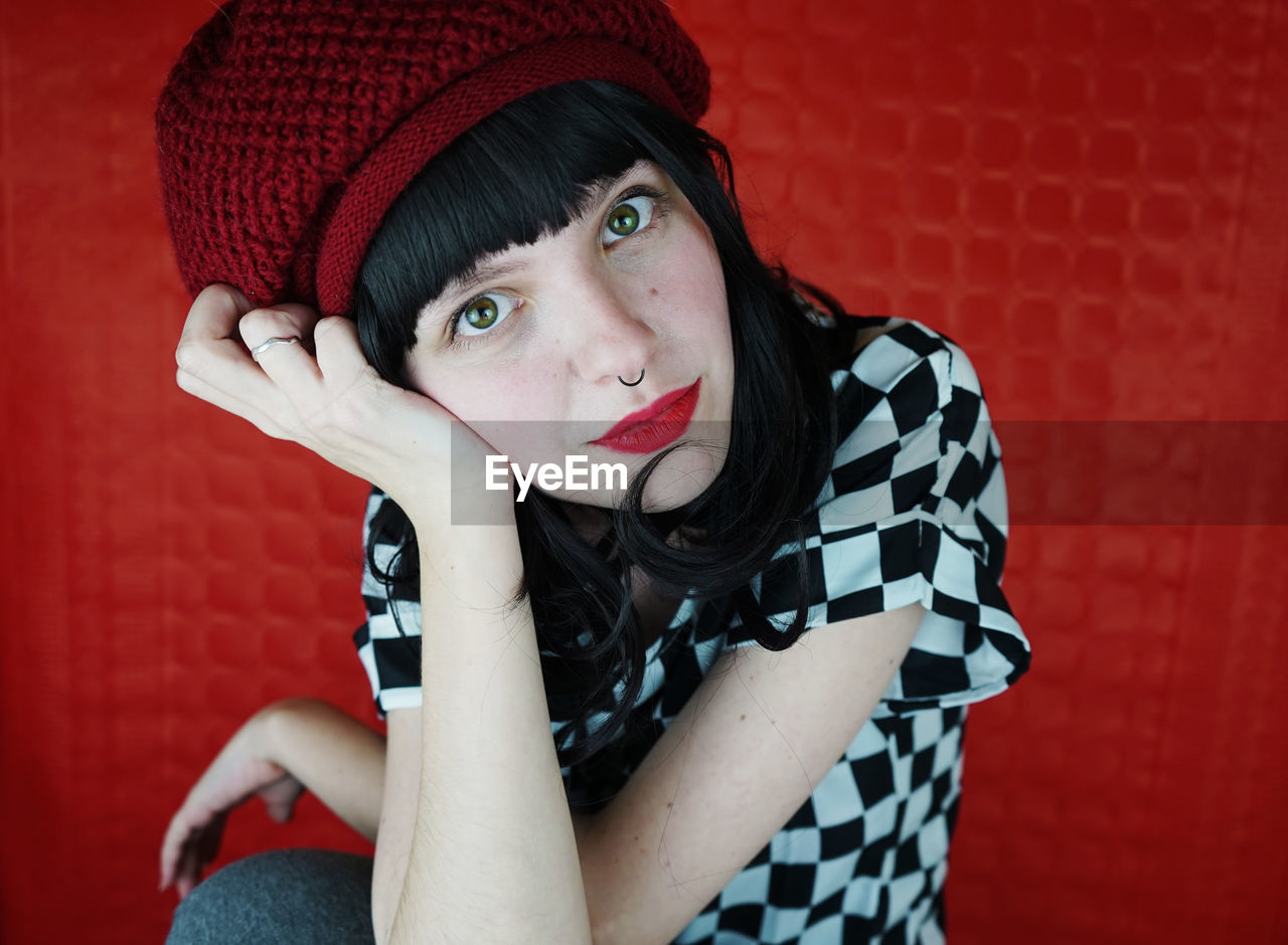 Close-up portrait of young woman sitting against red wall