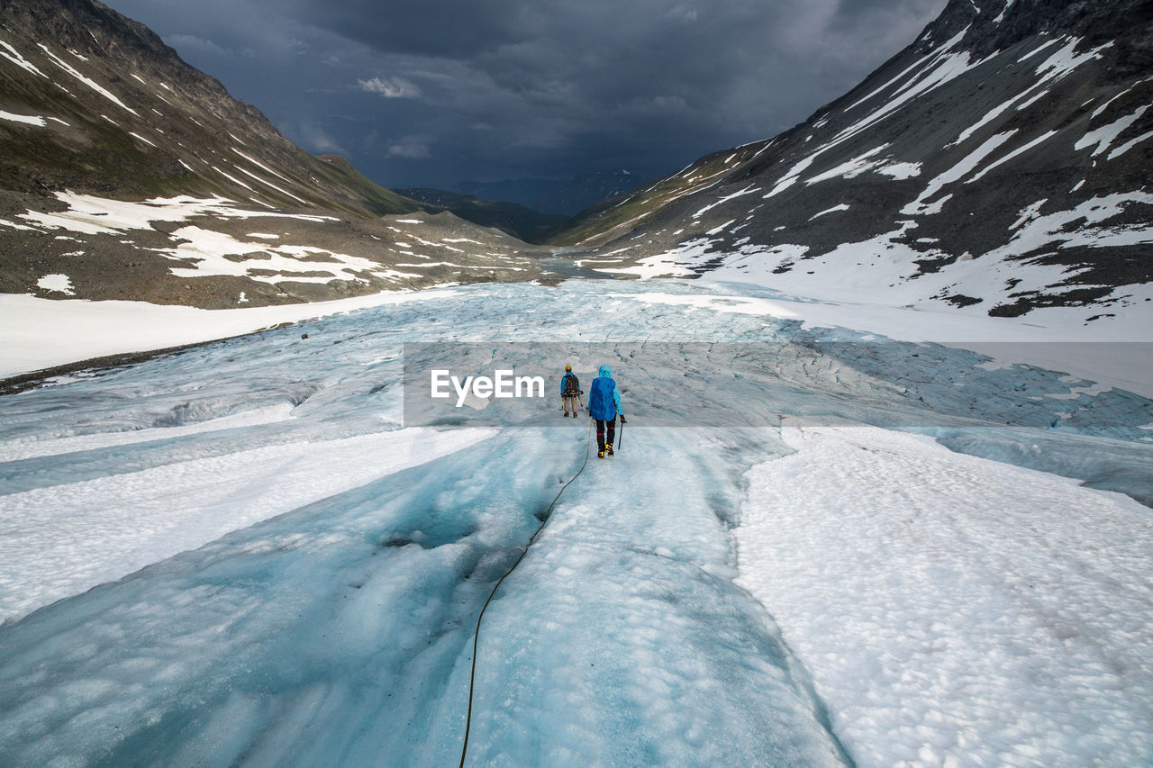 Rear view of people hiking on glacier by snowcapped mountains against sky