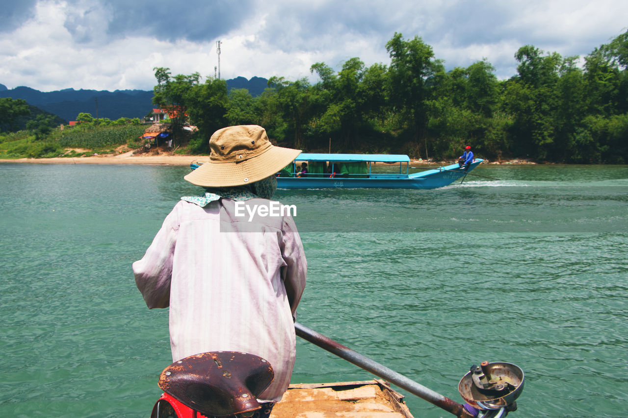 REAR VIEW OF MAN ON BOAT IN SEA AGAINST SKY