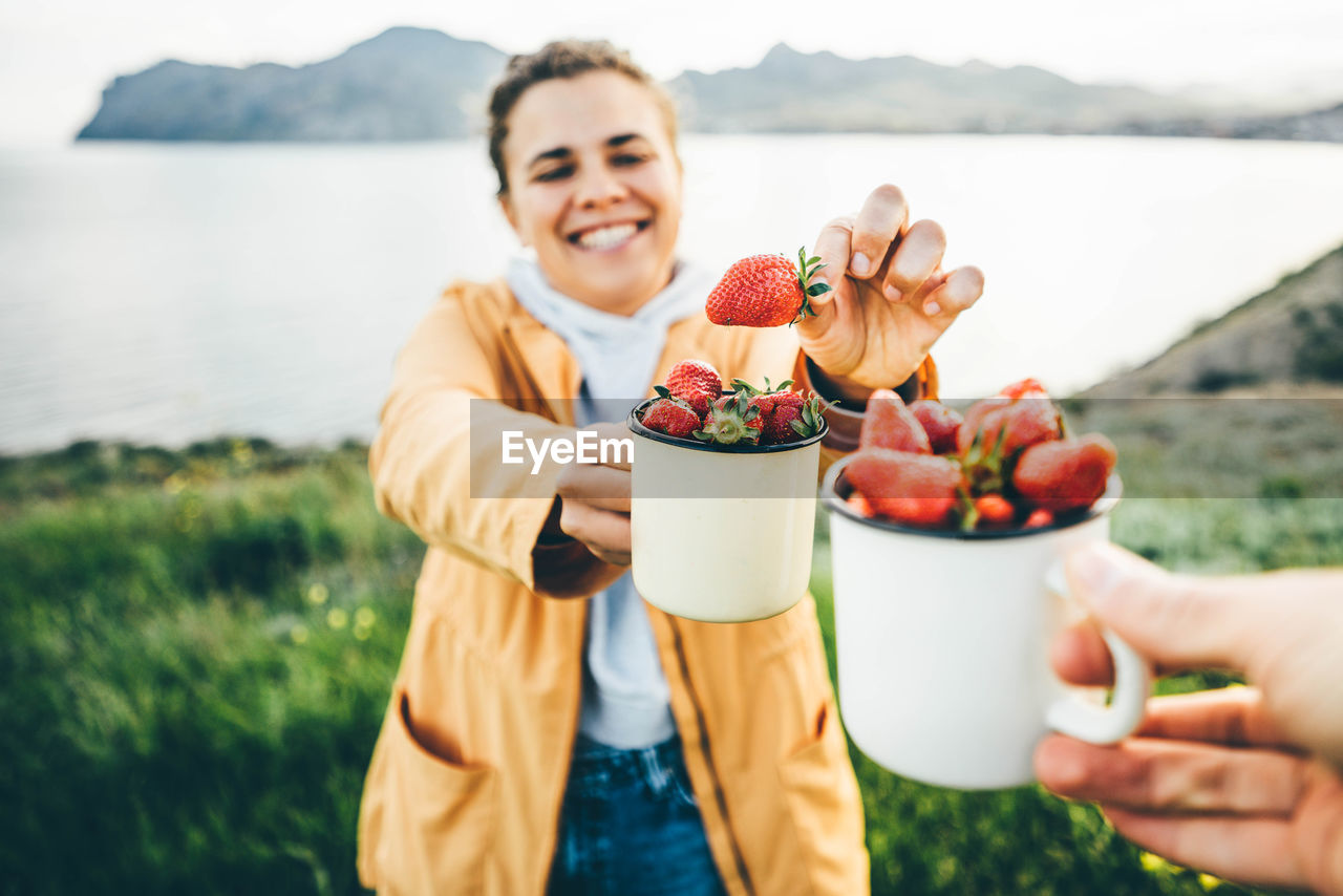 Couple smiling at camera while eating strawberries .