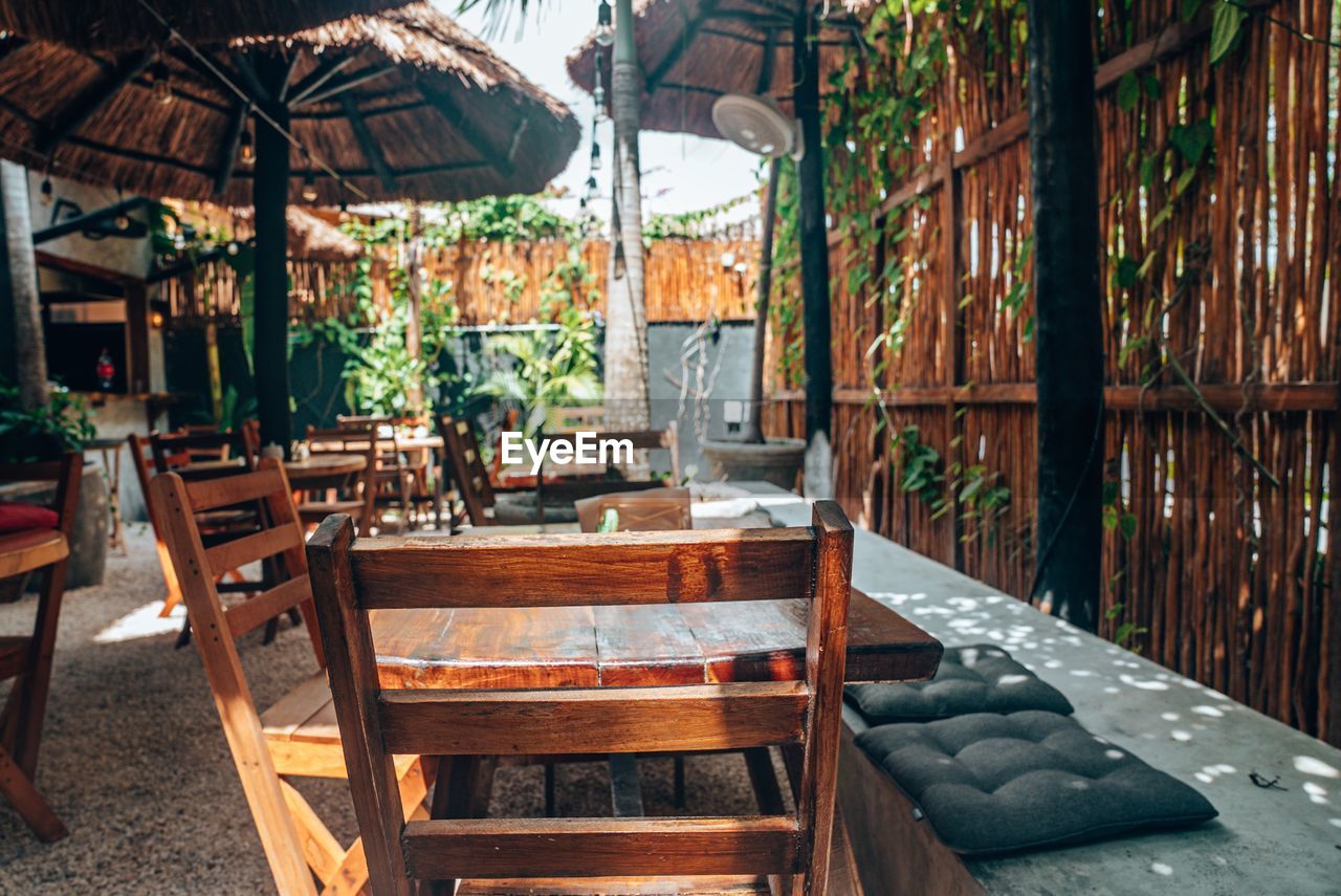 Empty wooden chairs and tables with straw umbrella at outdoor cafe