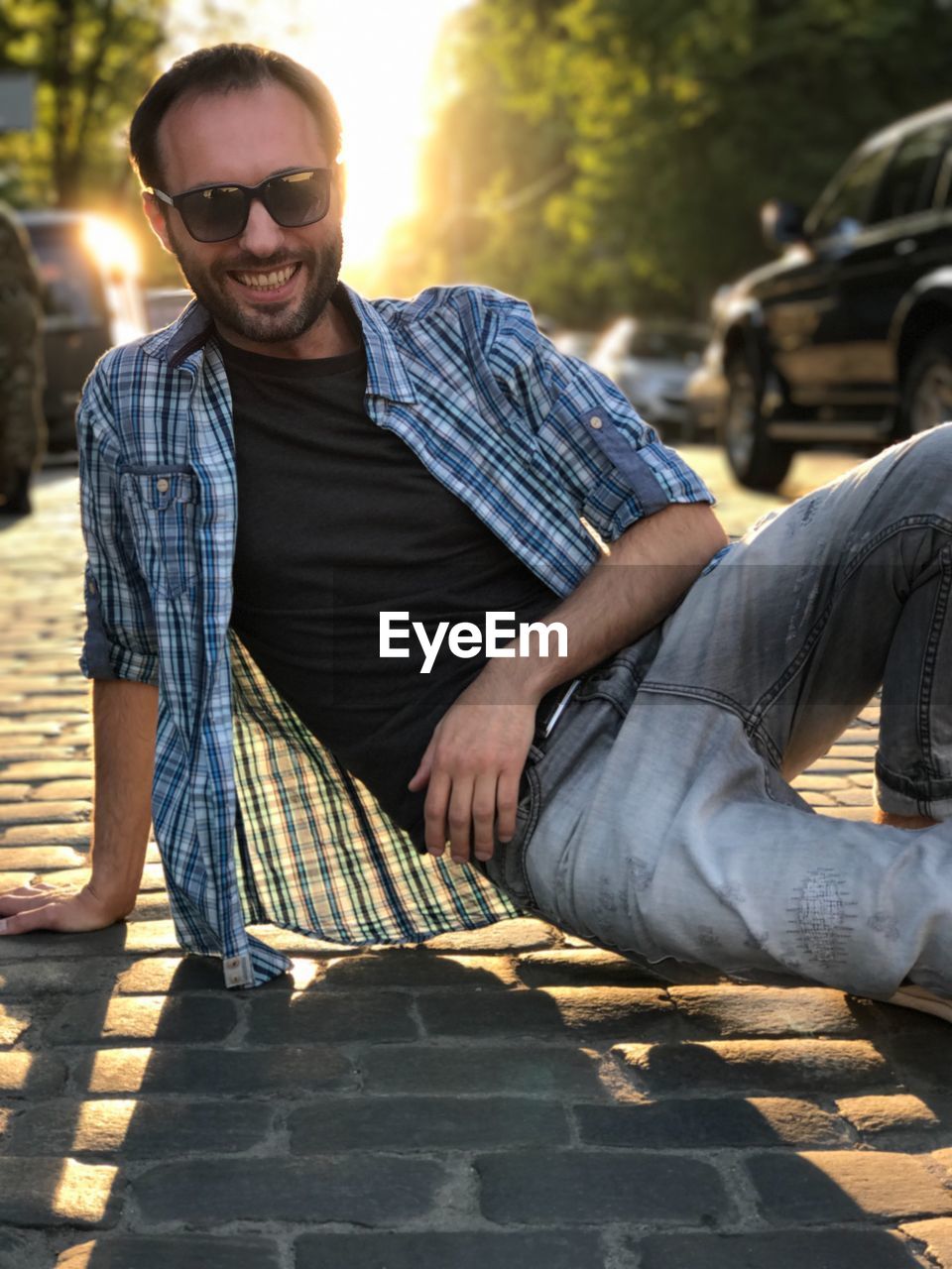 Portrait of smiling man wearing sunglasses on footpath during sunset