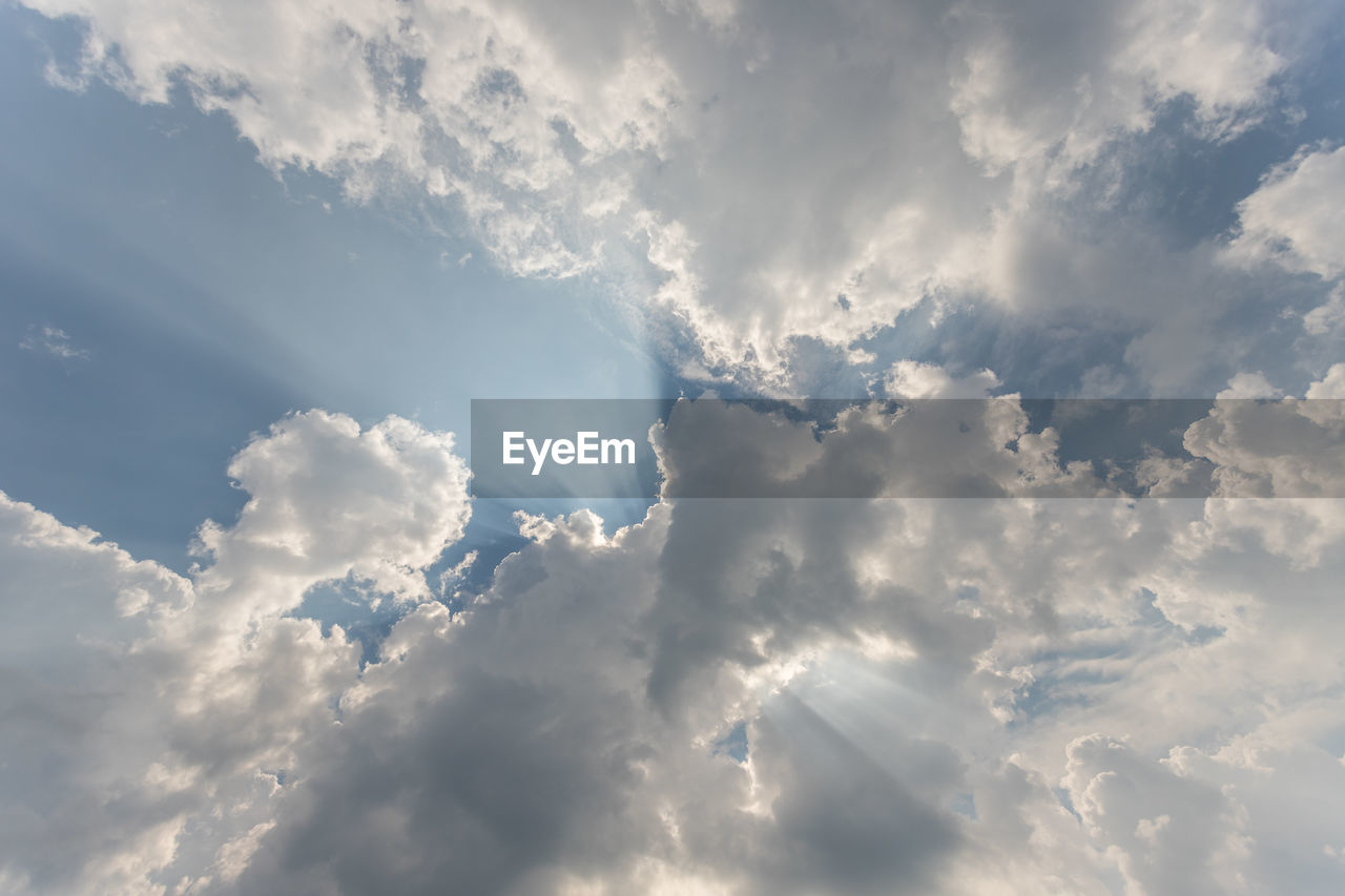 LOW ANGLE VIEW OF SUN STREAMING THROUGH CLOUDS IN SKY