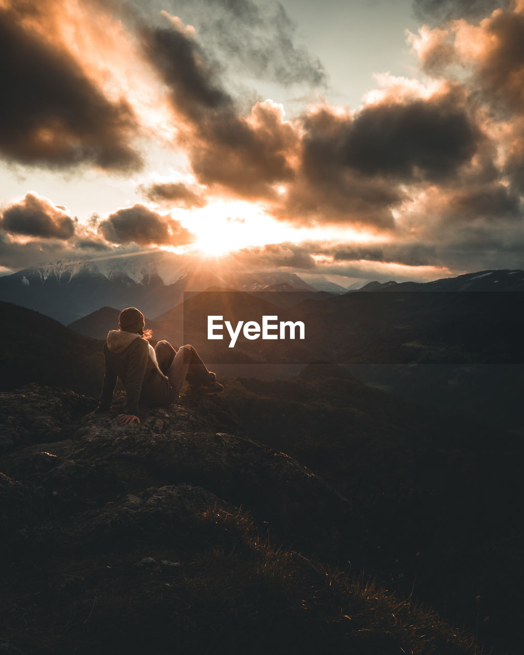 PEOPLE SITTING ON ROCK AT SUNSET