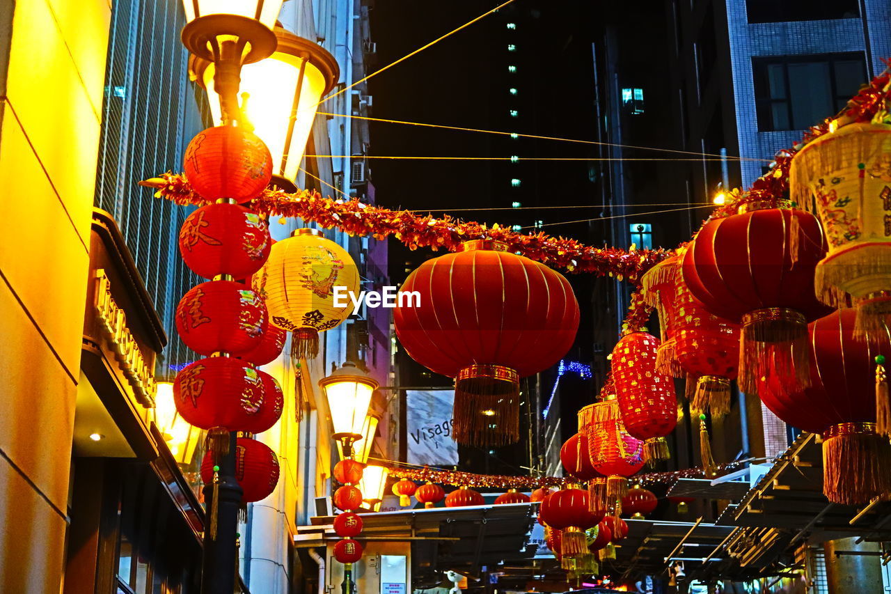 LOW ANGLE VIEW OF ILLUMINATED LANTERNS HANGING IN CITY