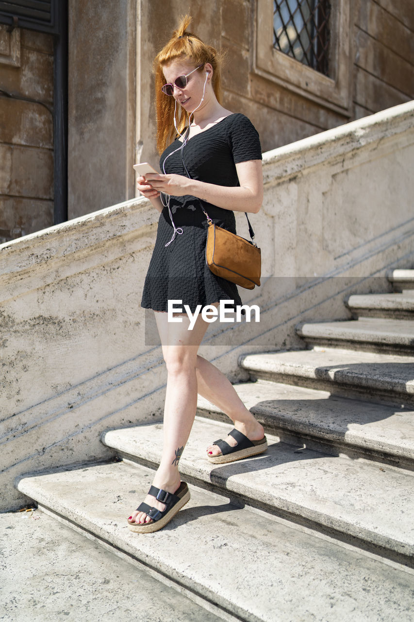 Fashion ginger girl reading the phone on stairs on a sunny summer day