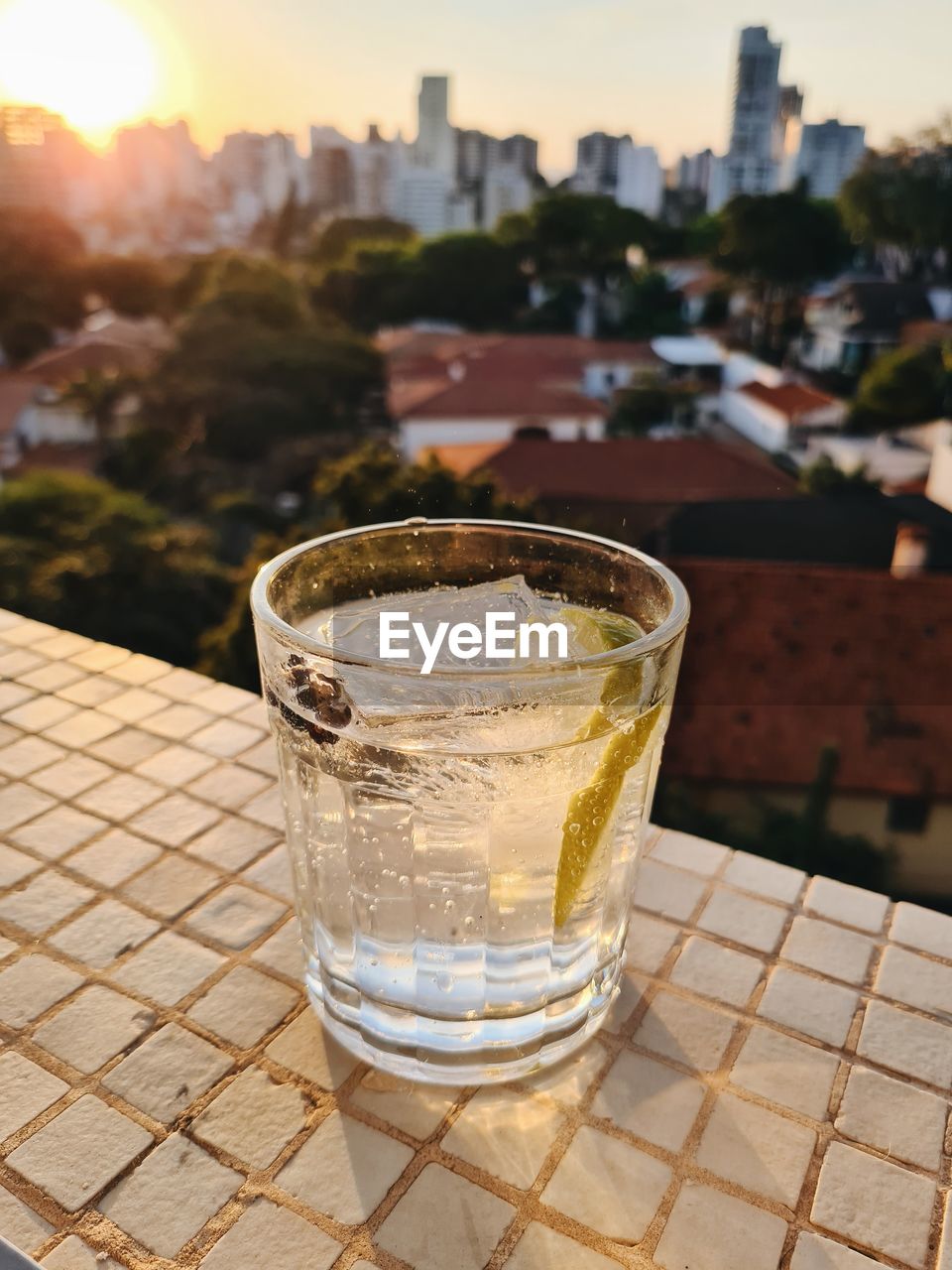 Close-up of gin tonic glass on windowsill at sunset