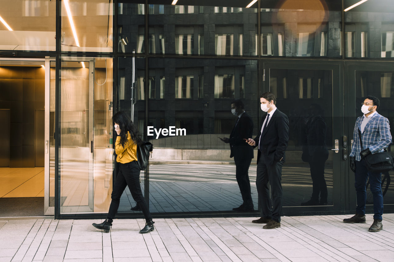 Business people with face masks standing in line outside office building