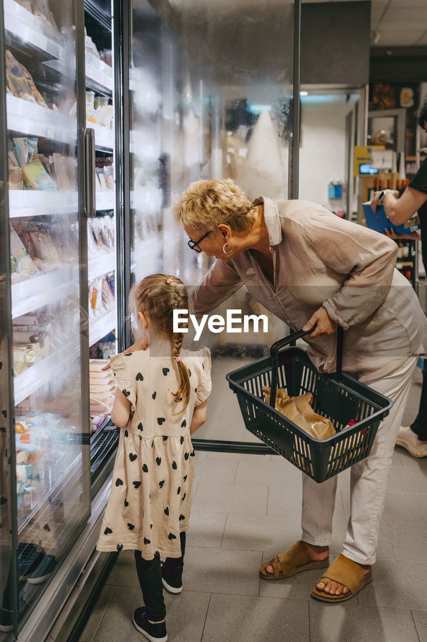 Girl buying frozen foods from refrigerated section with grandmother at grocery store