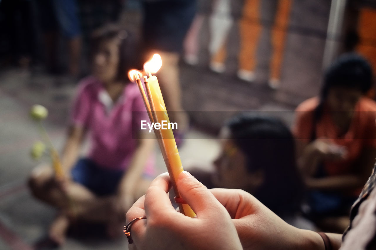 Cropped image of woman holding lit candle with incense sticks in temple