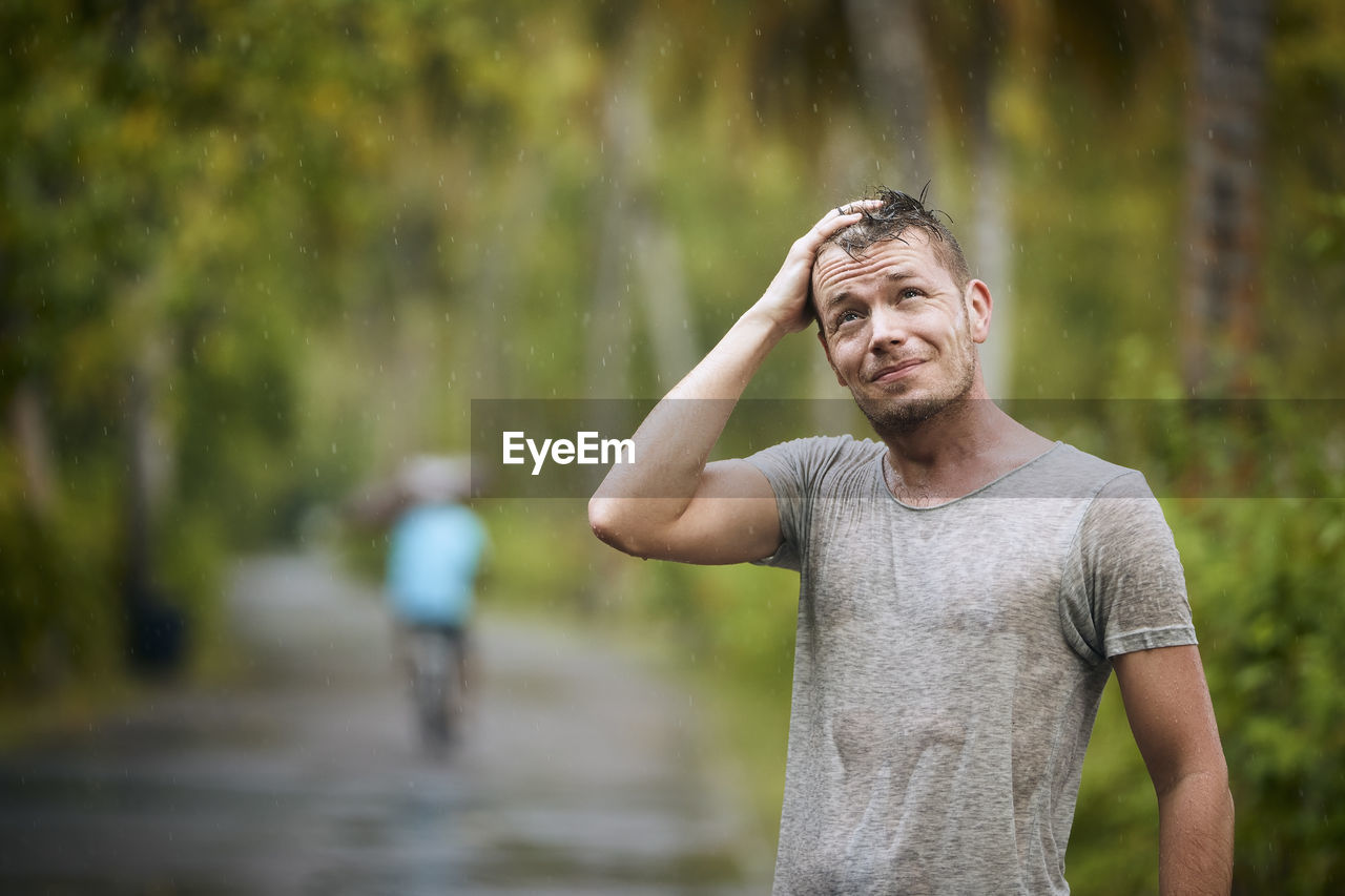 Portrait of drenched young man enjoying heavy rain in nature.