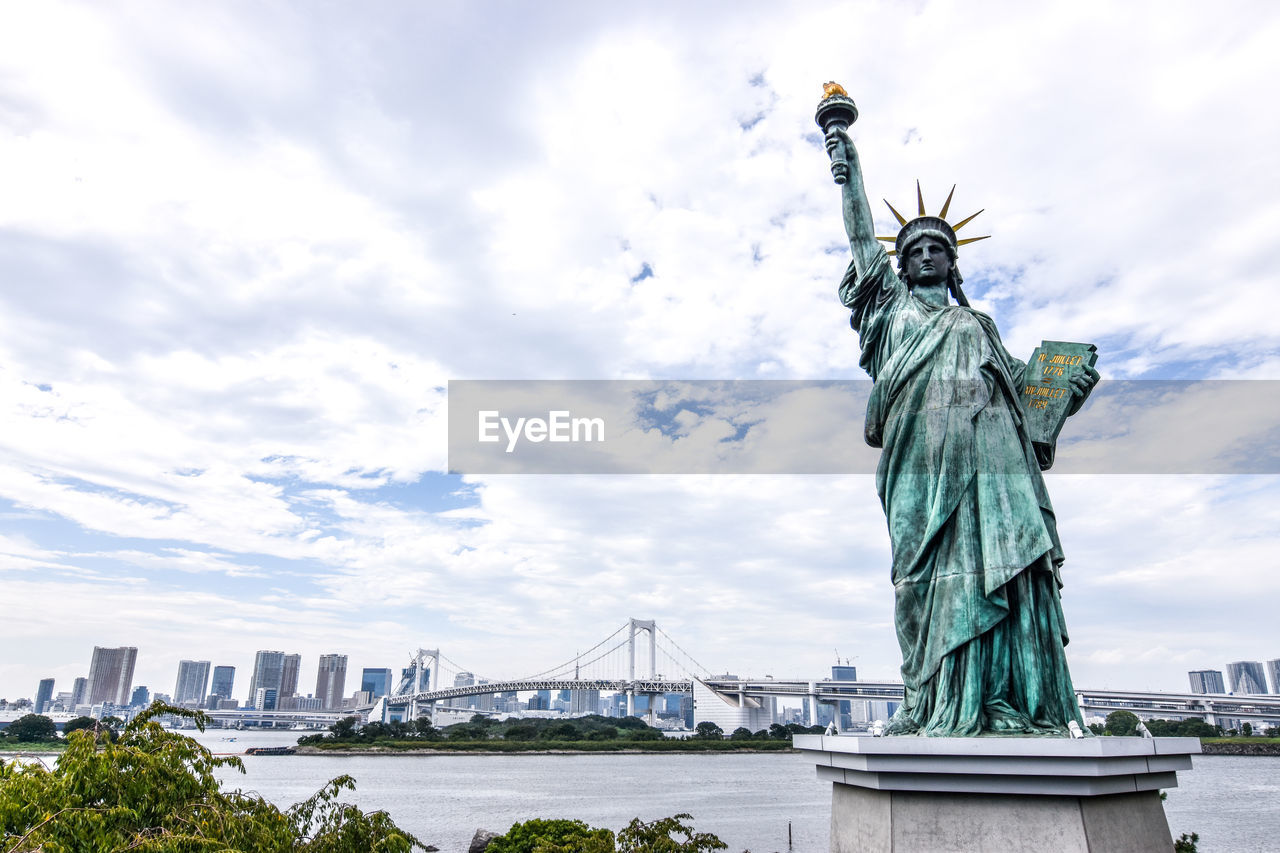 Statue of liberty in city against cloudy sky