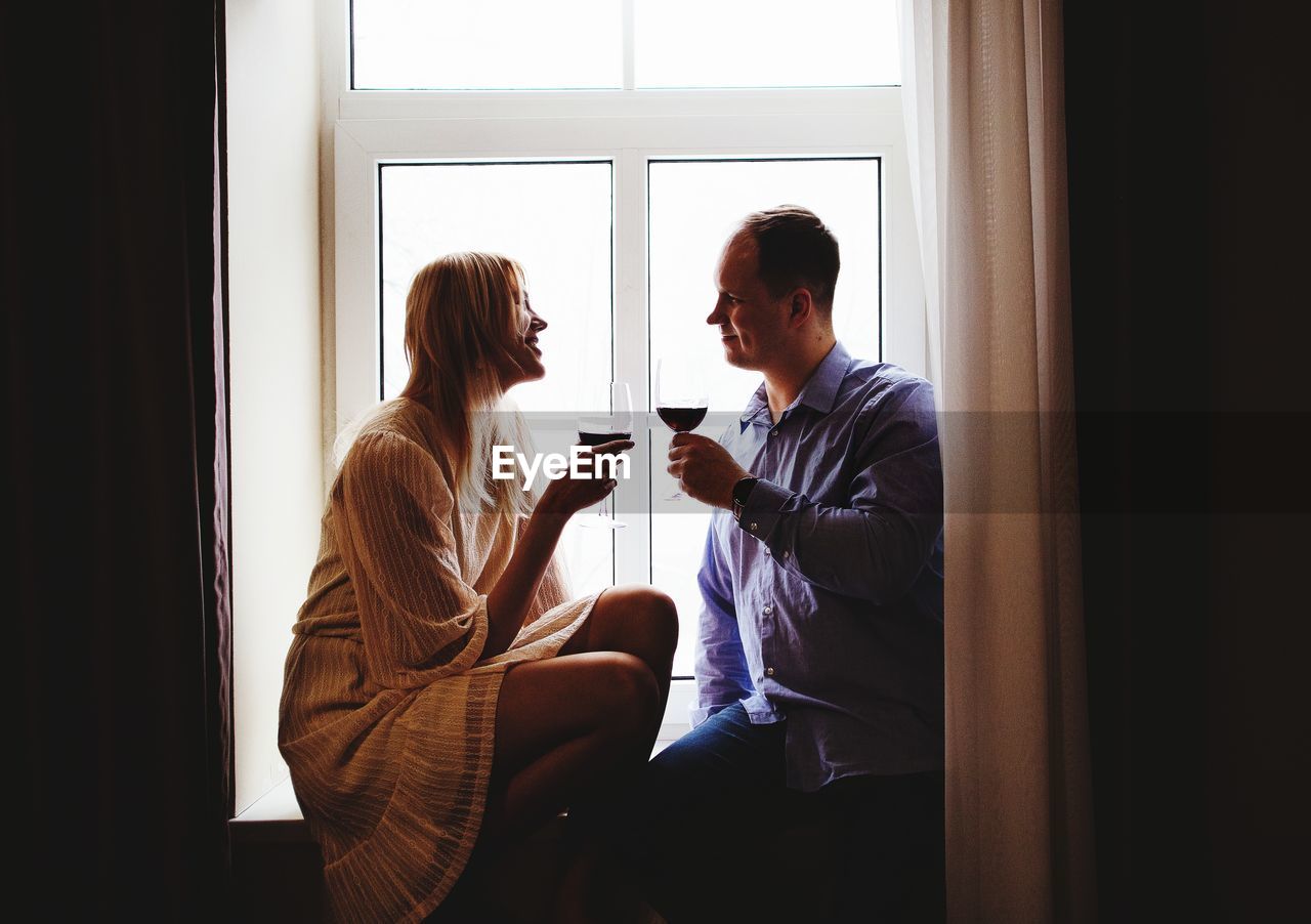 Couple holding drink while sitting by window