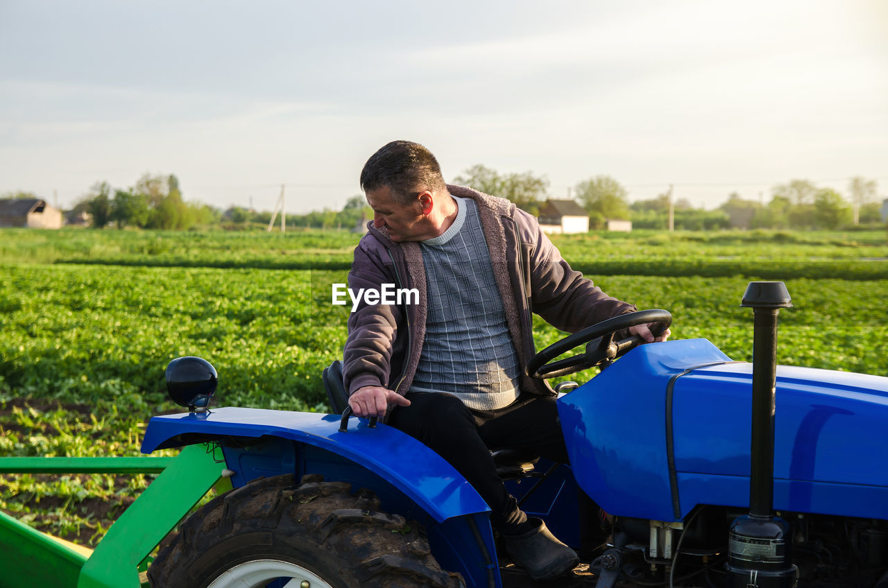 A farmer on a tractor monitors the operation of equipment for harvesting potatoes. farming farmland