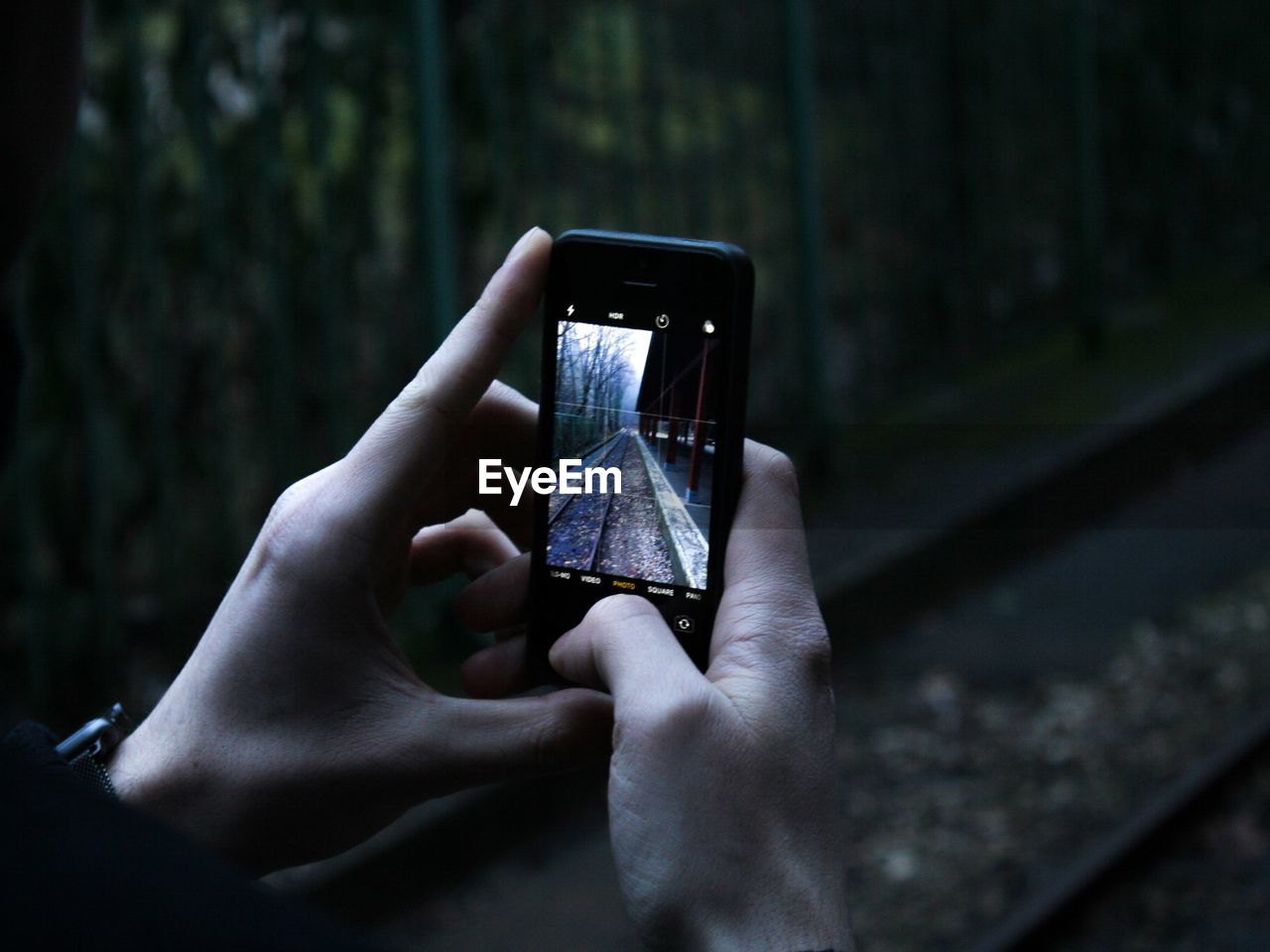 Cropped image of person photographing railroad tracks through mobile phone