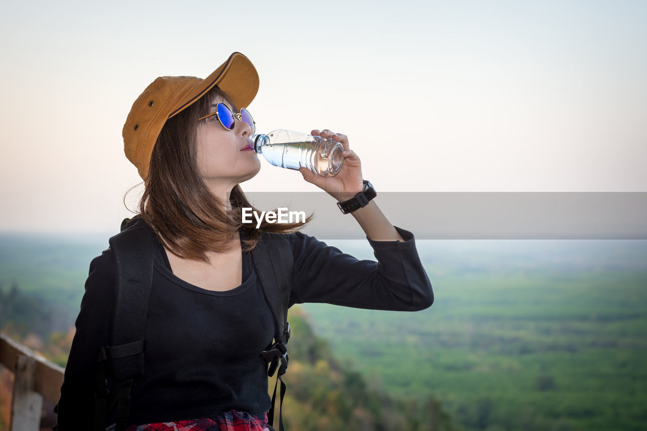 Woman drinking water from bottle against landscape