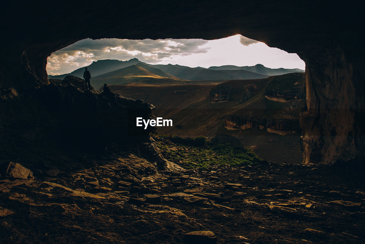 Man standing at cave against mountains during sunset