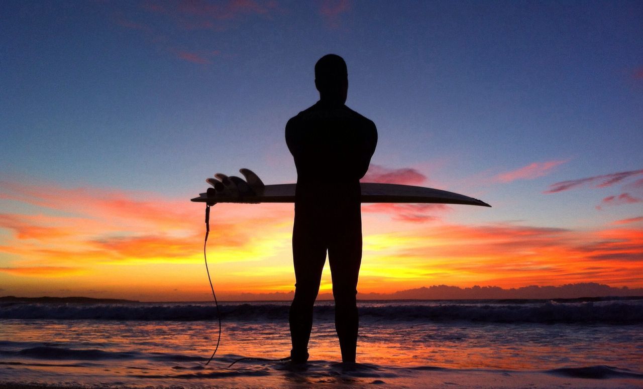 Silhouette man carrying surfboard on beach