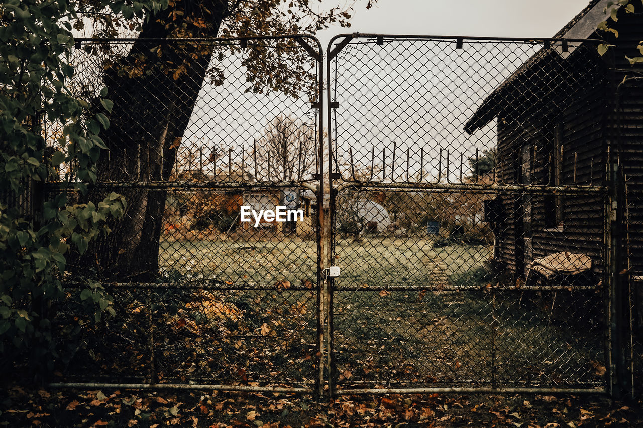 FENCE BY TREES AND BUILDINGS AGAINST SKY SEEN THROUGH CHAINLINK RAILING