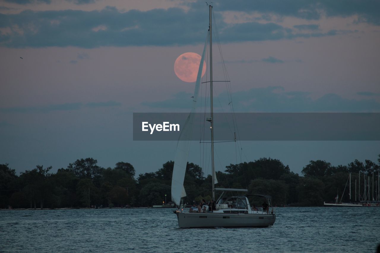 SAILBOATS SAILING ON RIVER AGAINST SKY AT SUNSET