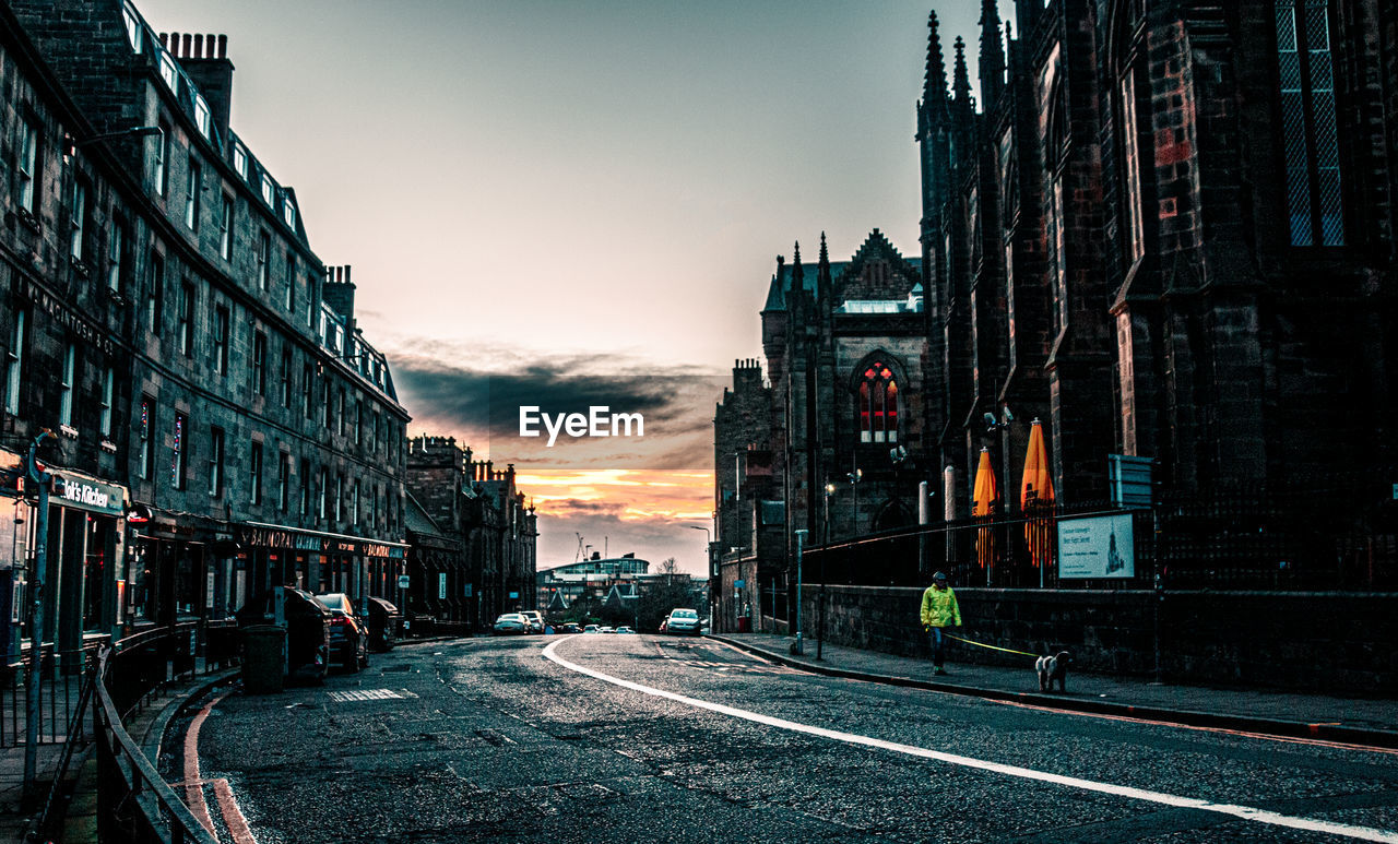 ROAD BY BUILDINGS AGAINST SKY DURING SUNSET