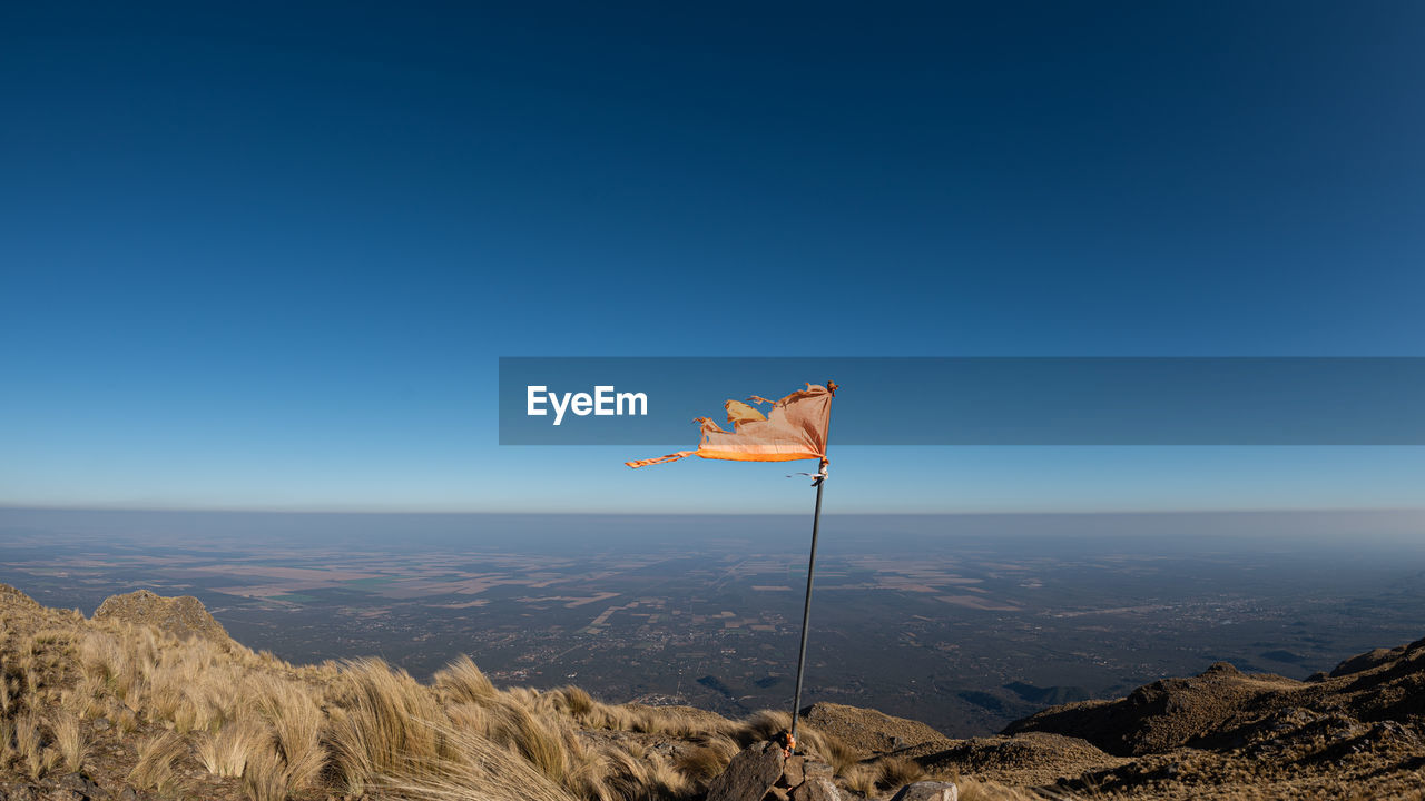 FLAG ON LANDSCAPE AGAINST CLEAR BLUE SKY