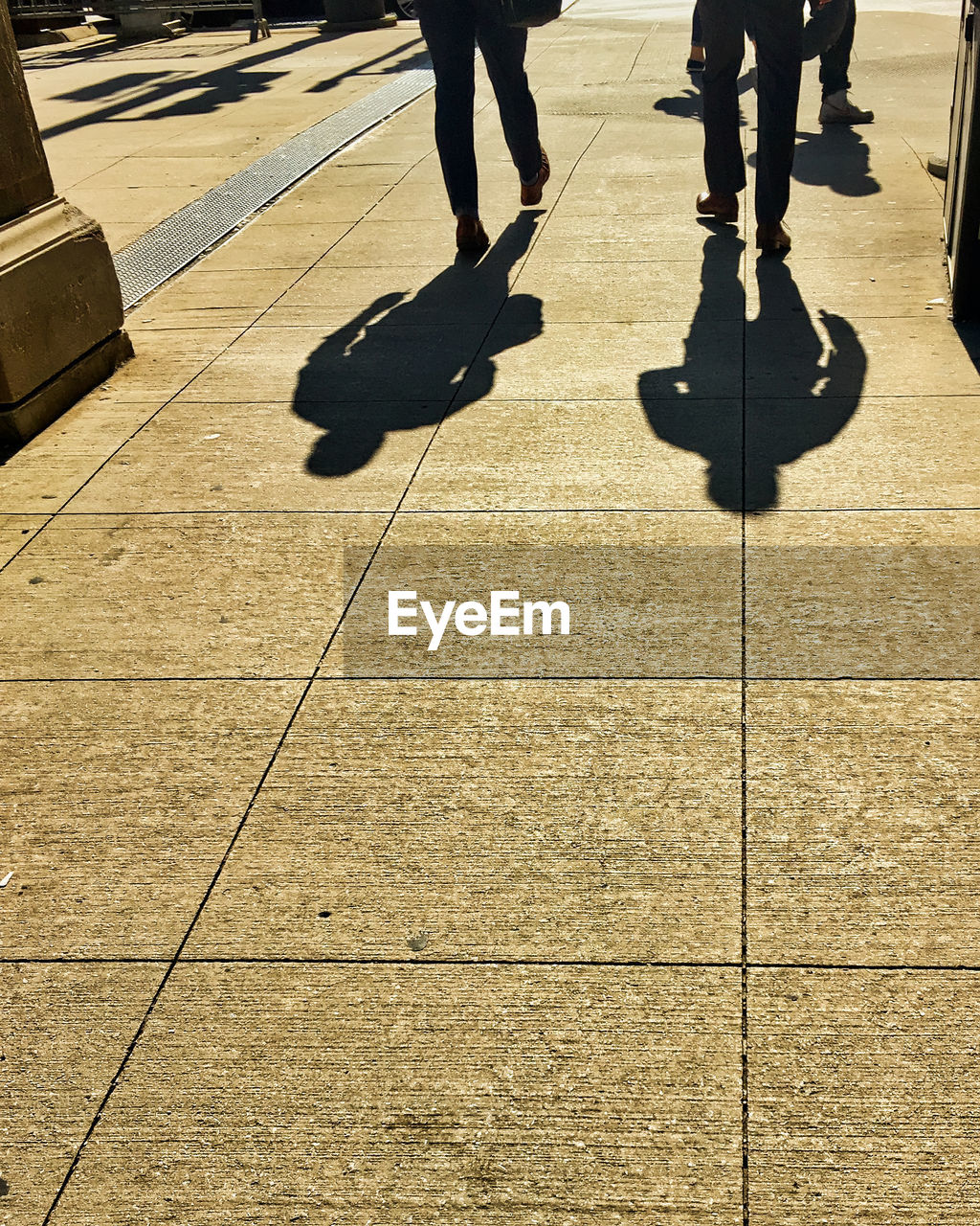 Low section of people walking on footpath in city during sunny day