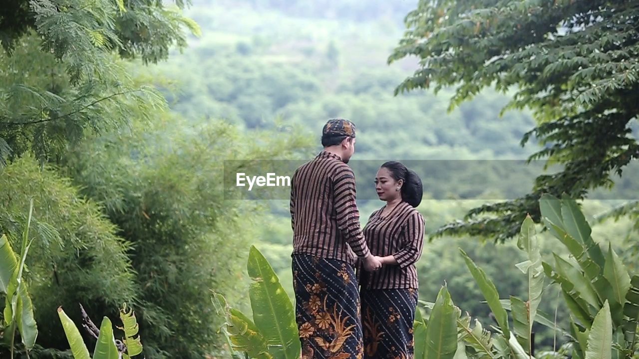 PEOPLE STANDING BY TREE AGAINST PLANTS