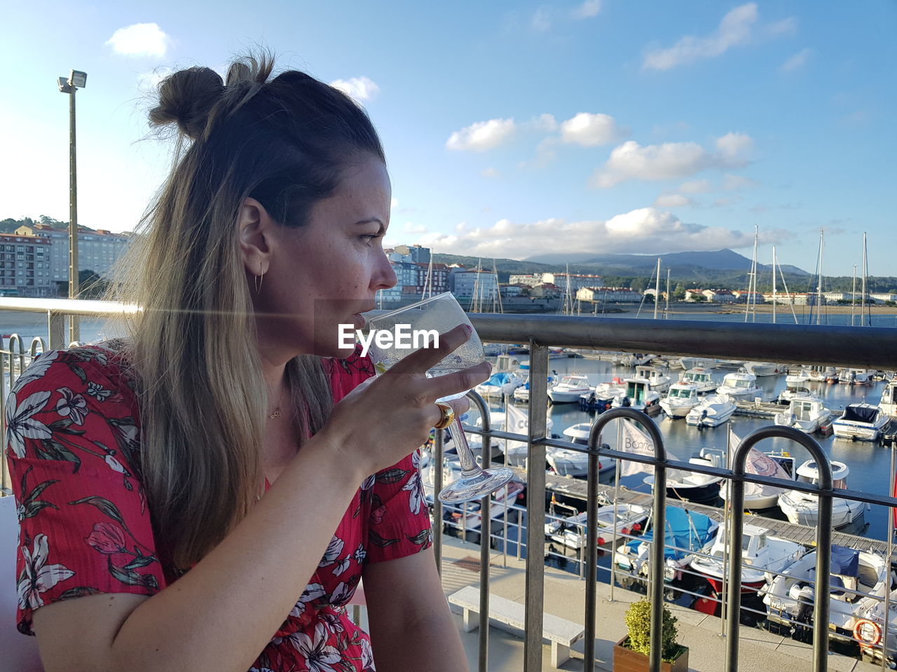 Young woman drinking wine against harbor