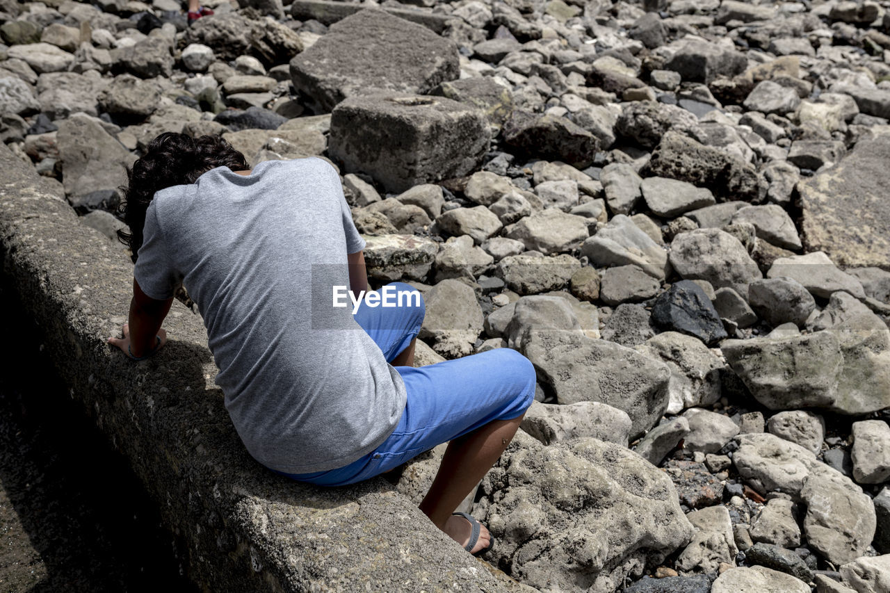 Rear view of man sitting on retaining wall