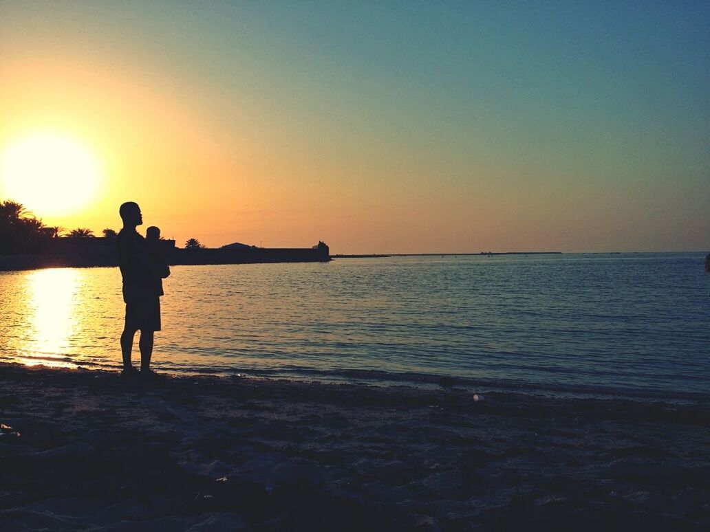 Silhouette man holding baby at beach during sunset