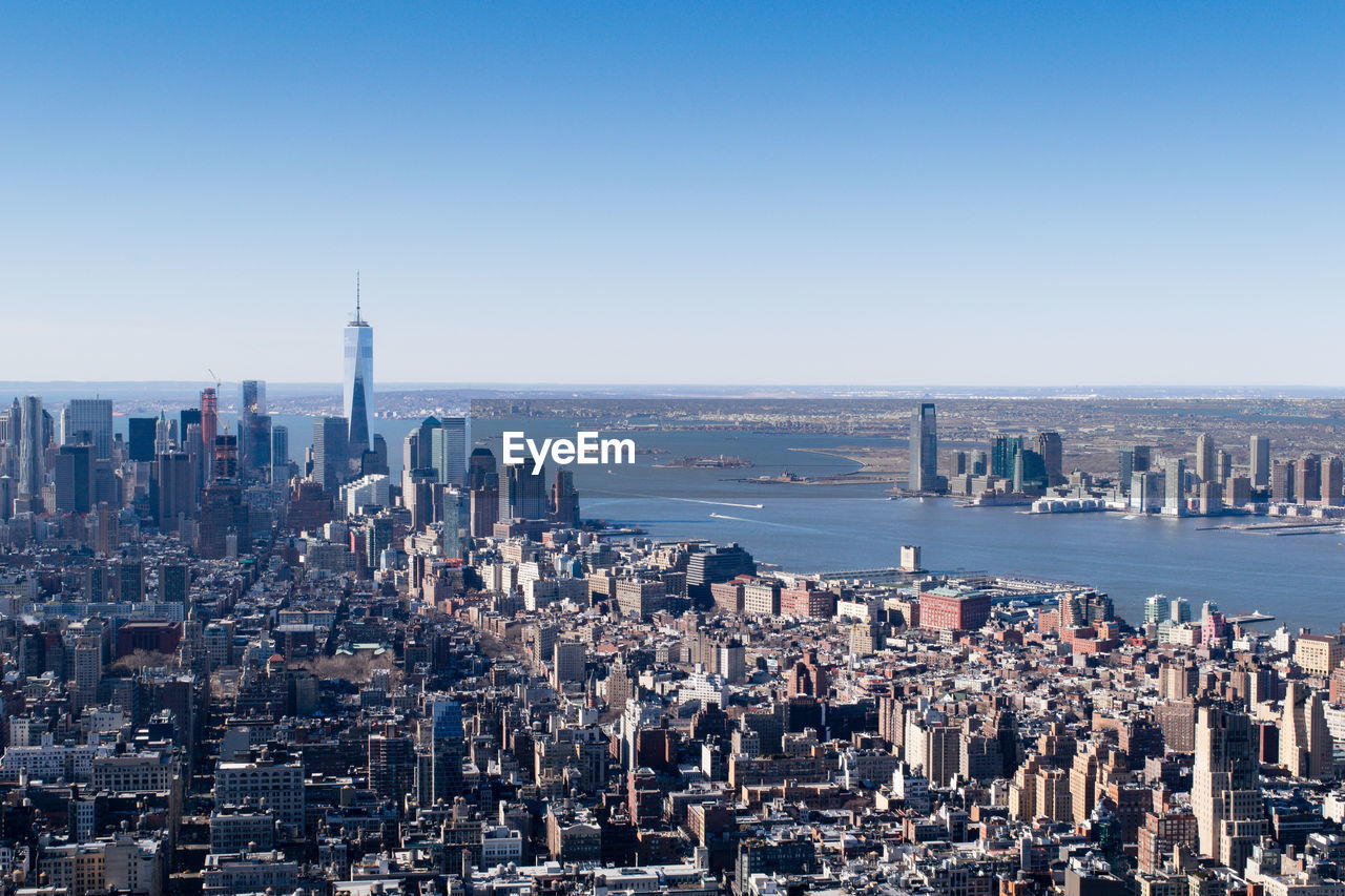 One world trade center amidst cityscape by hudson river against clear sky