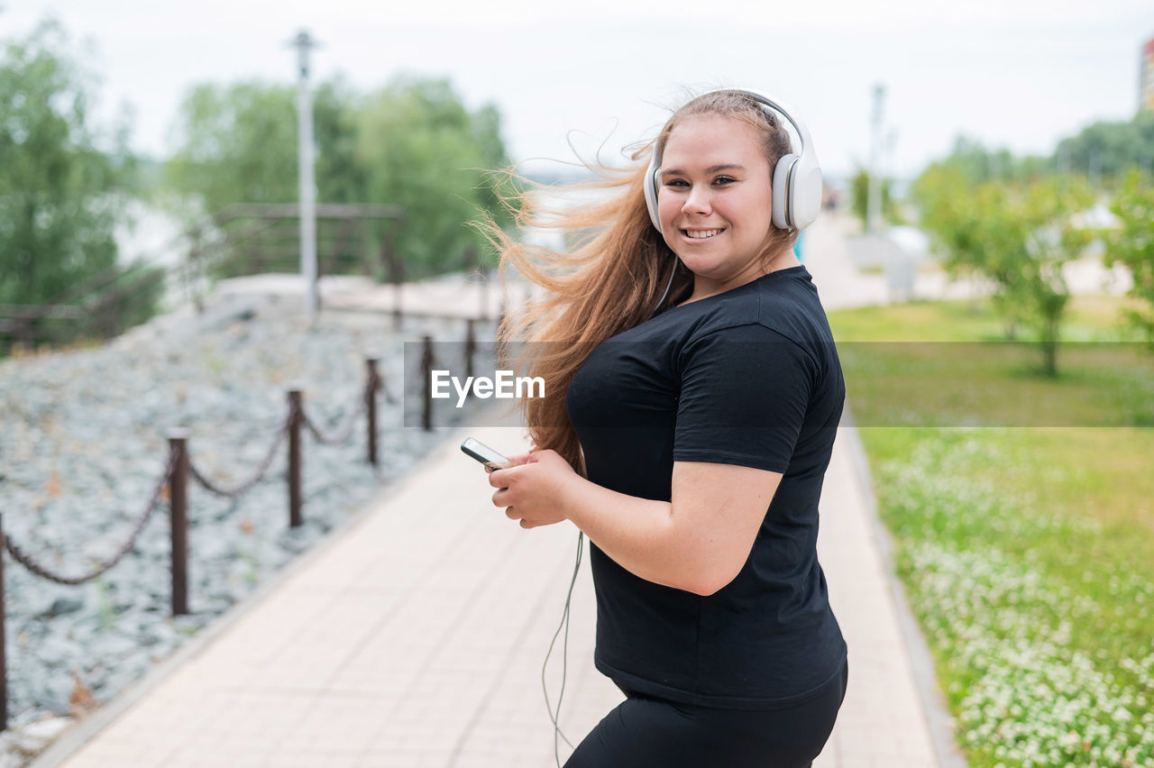 PORTRAIT OF SMILING YOUNG WOMAN USING PHONE WHILE STANDING ON MOBILE
