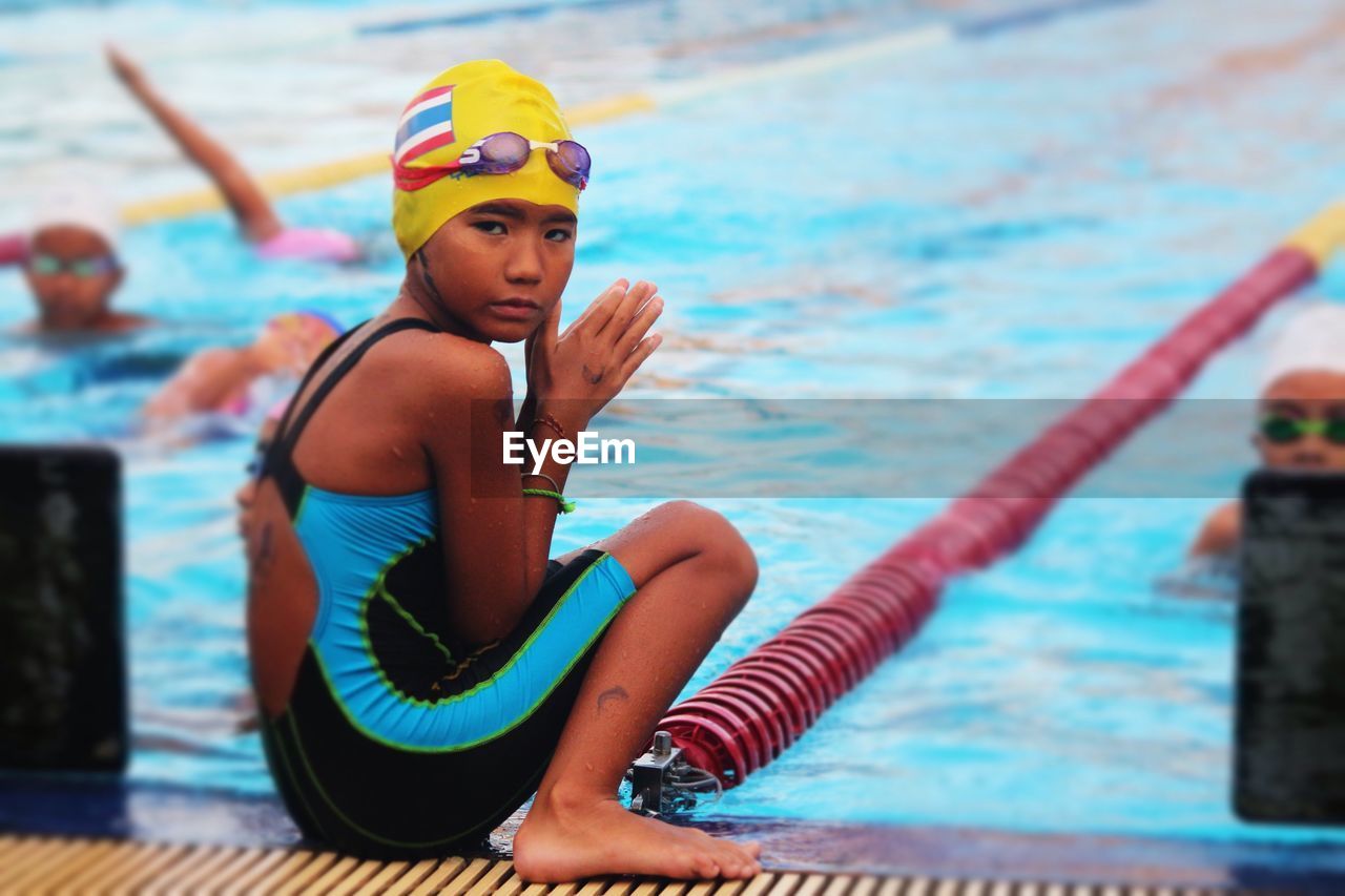 Portrait of girl wearing swimwear sitting at poolside