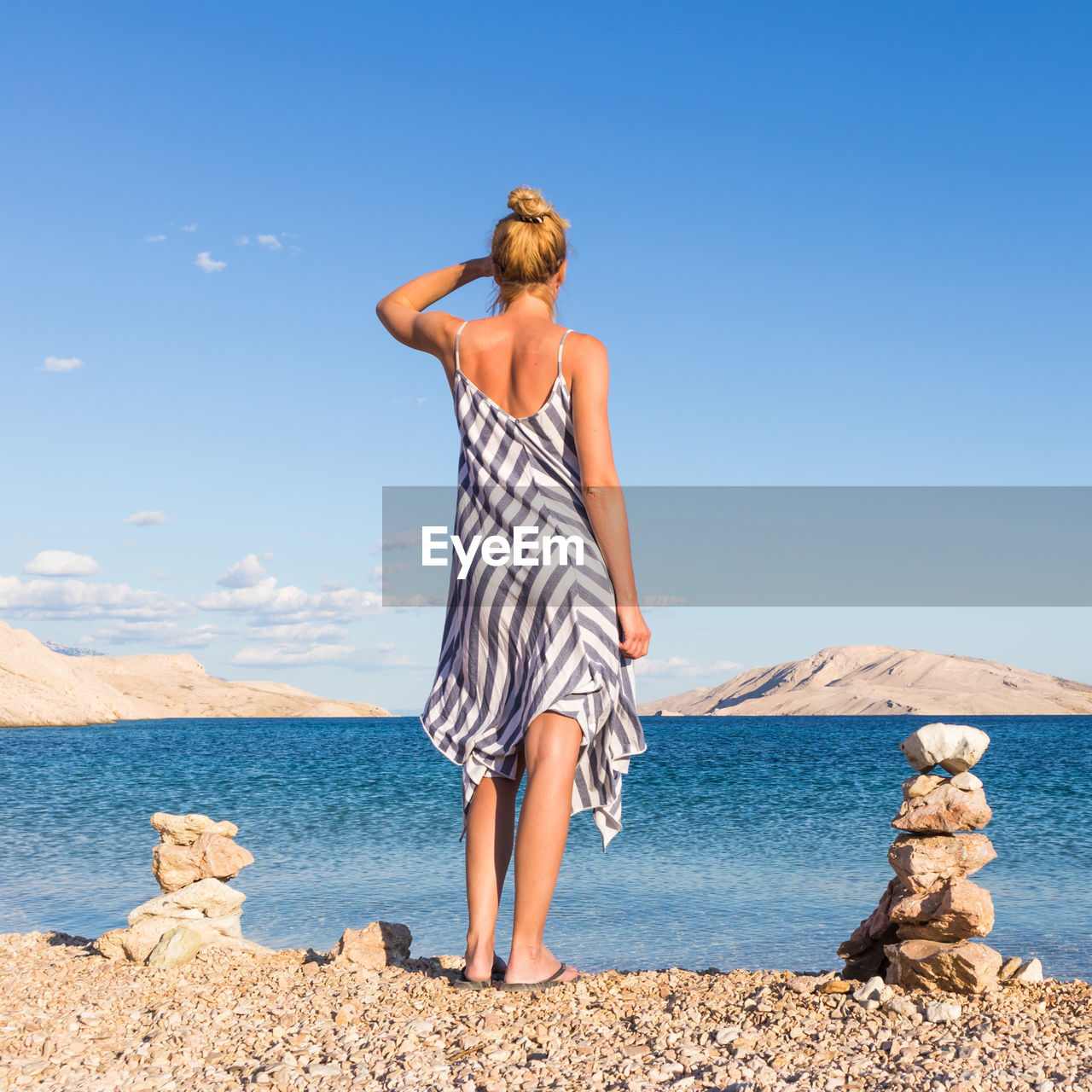 REAR VIEW OF WOMAN STANDING ON BEACH AGAINST SKY