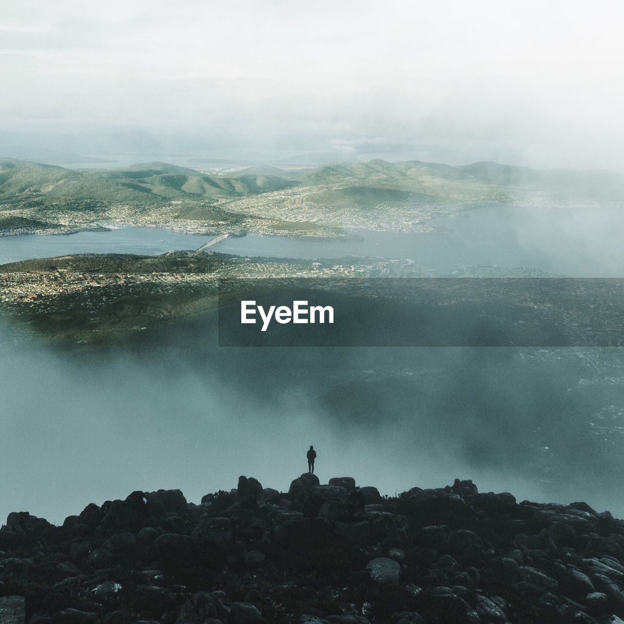 Person standing on rocks by landscape against sky during foggy weather