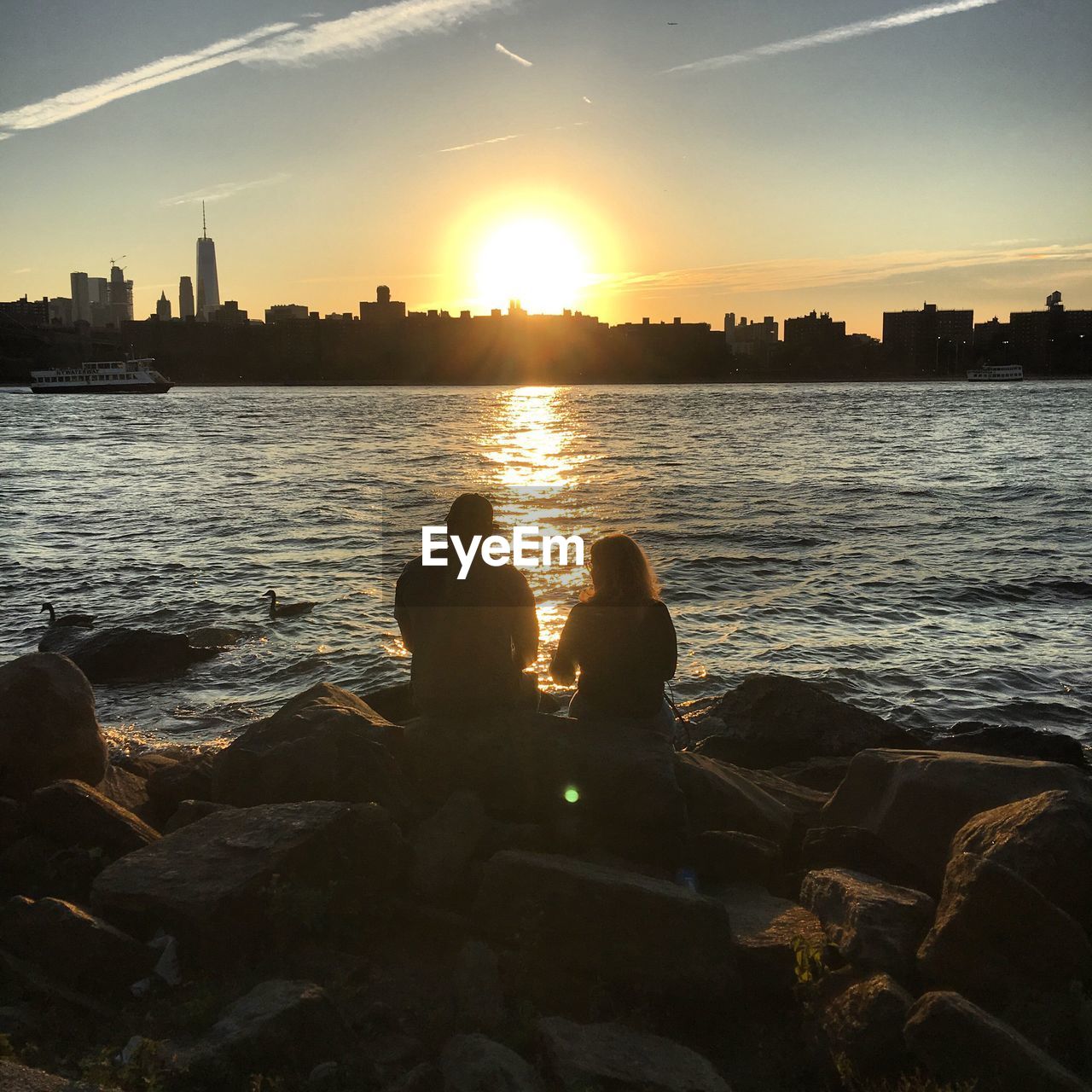 REAR VIEW OF SILHOUETTE MAN SITTING ON SHORE AGAINST SKY