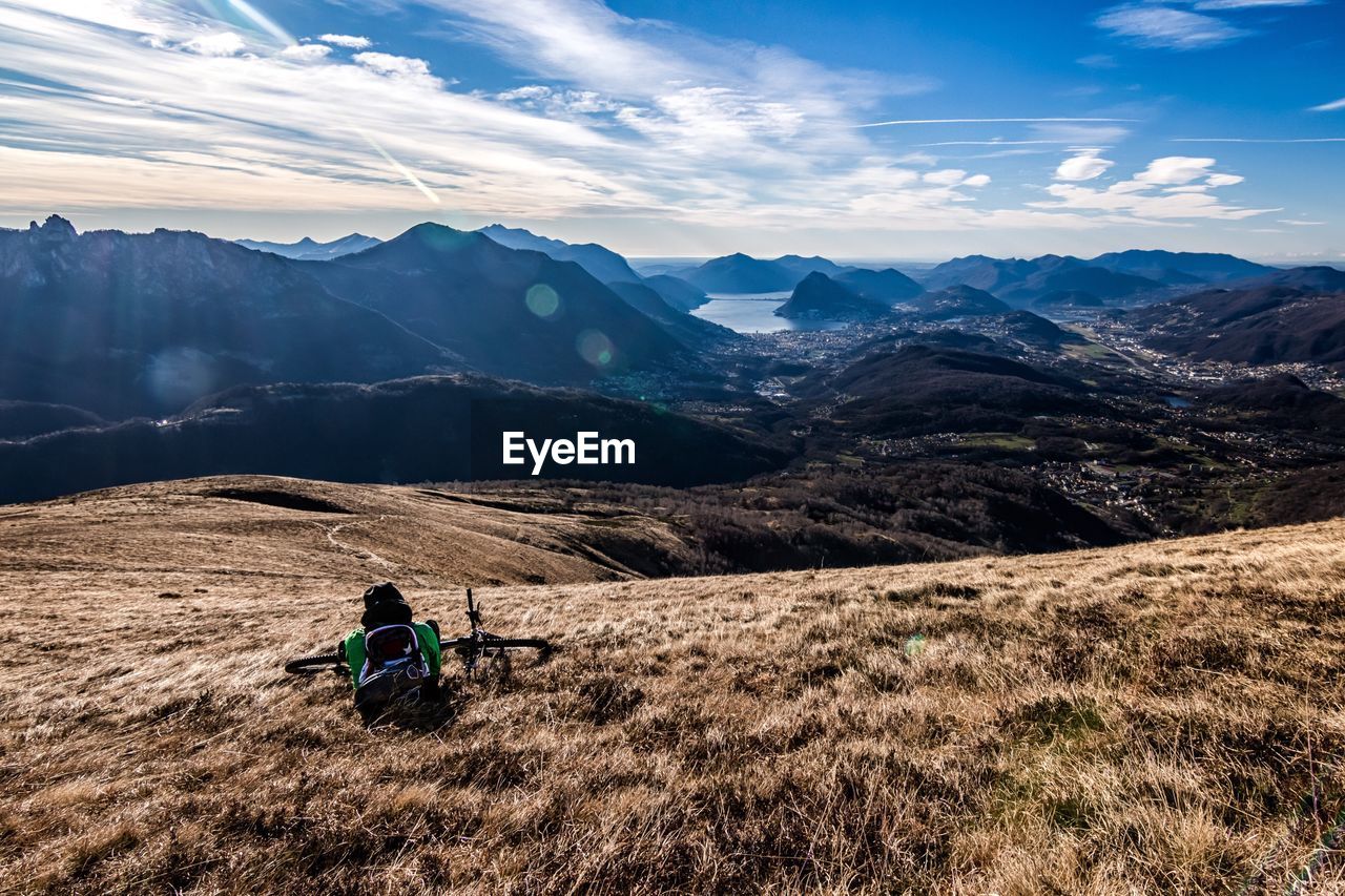 Rear view of man with backpack and bicycle sitting on mountain against sky