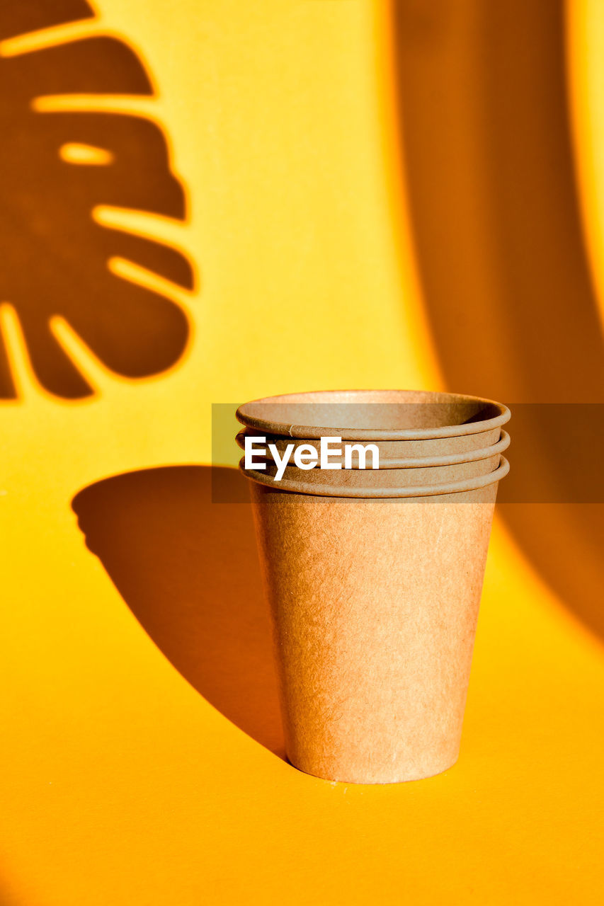 Paper coffee containers on yellow background with hard shadows of palm leaf. paper cups. copy space.