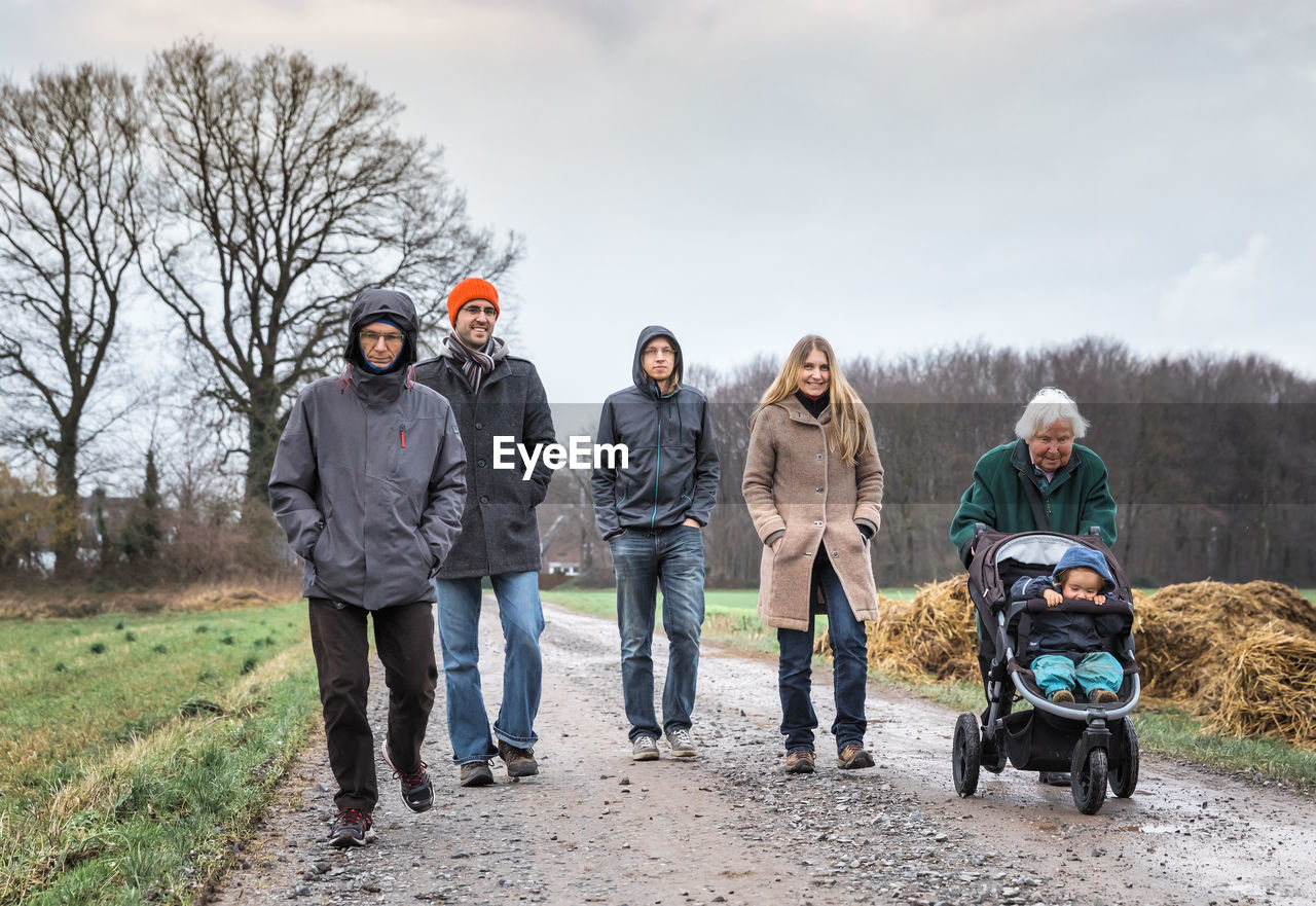 Family walking on road against sky during winter