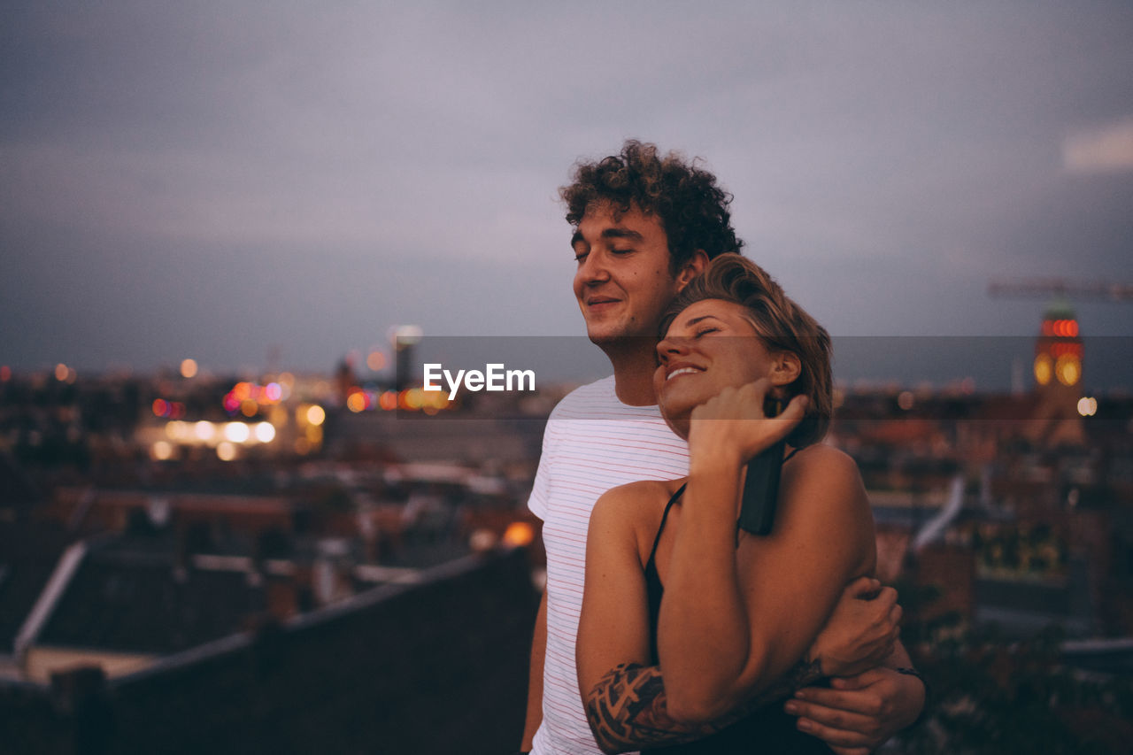 Loving couple embracing while standing on terrace against sky at dusk