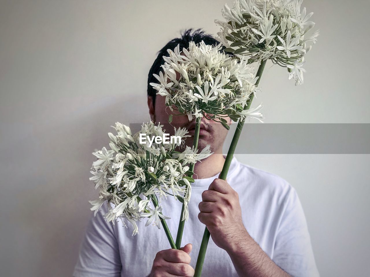 Man holding 3 stalks of white, african lilies flowers against white background.