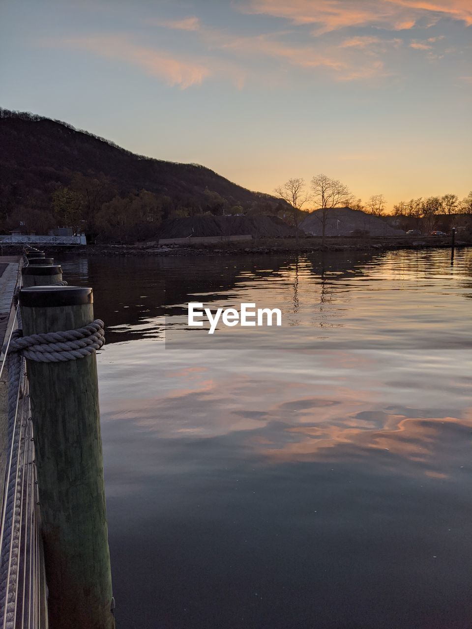 WOODEN POST IN LAKE AGAINST SKY DURING SUNSET